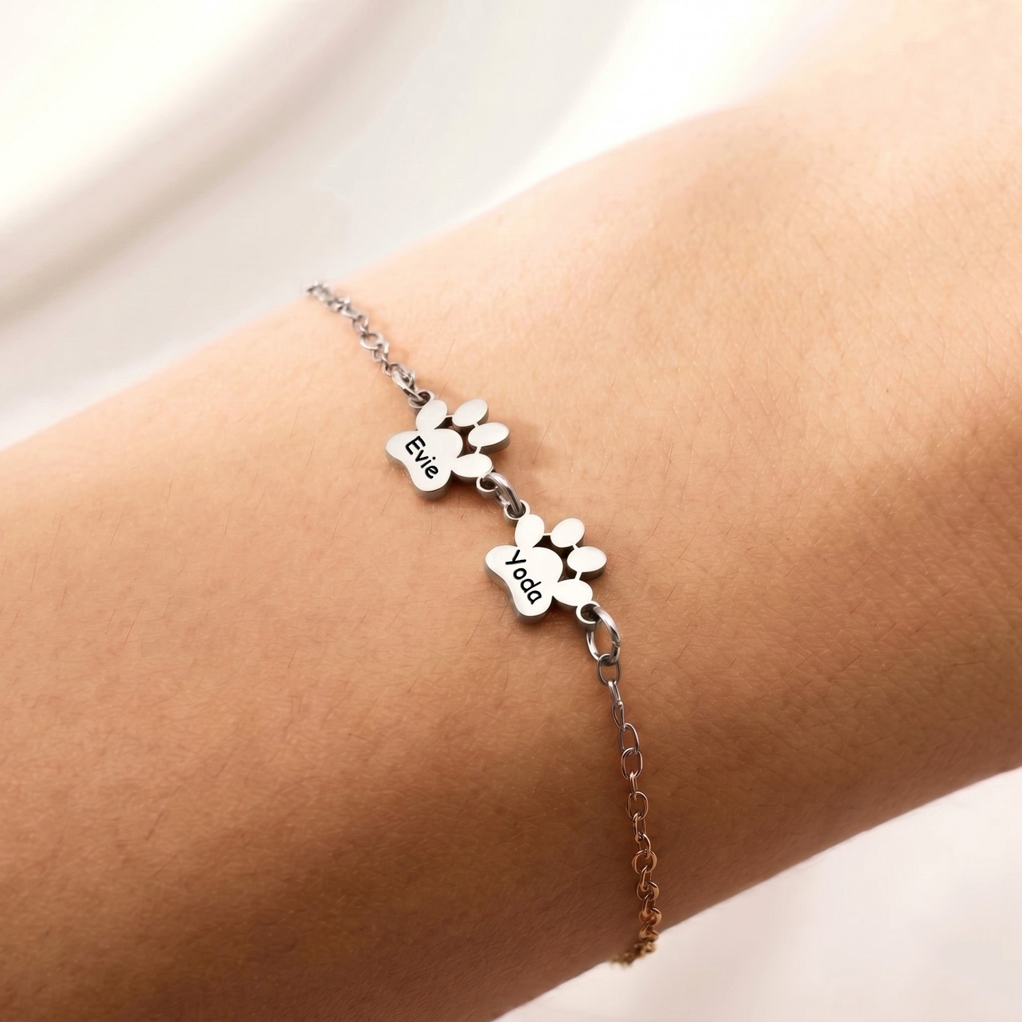 Silver rhodium paw print bracelet with two engraved name charms worn on the wrist
