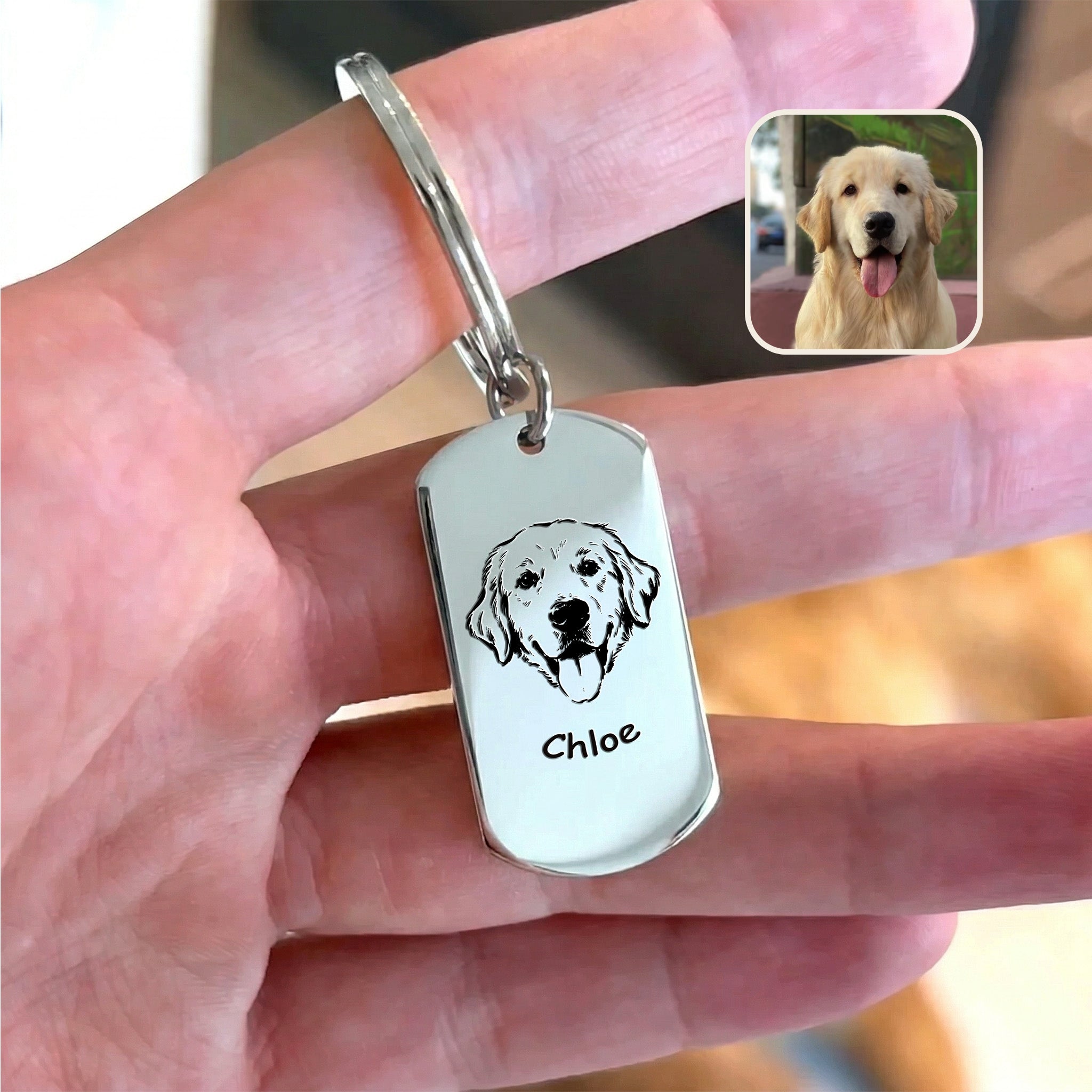 Rhodium plated pet portrait dog tag keychain held in hand beside original dog reference photo, warm indoor styled scene