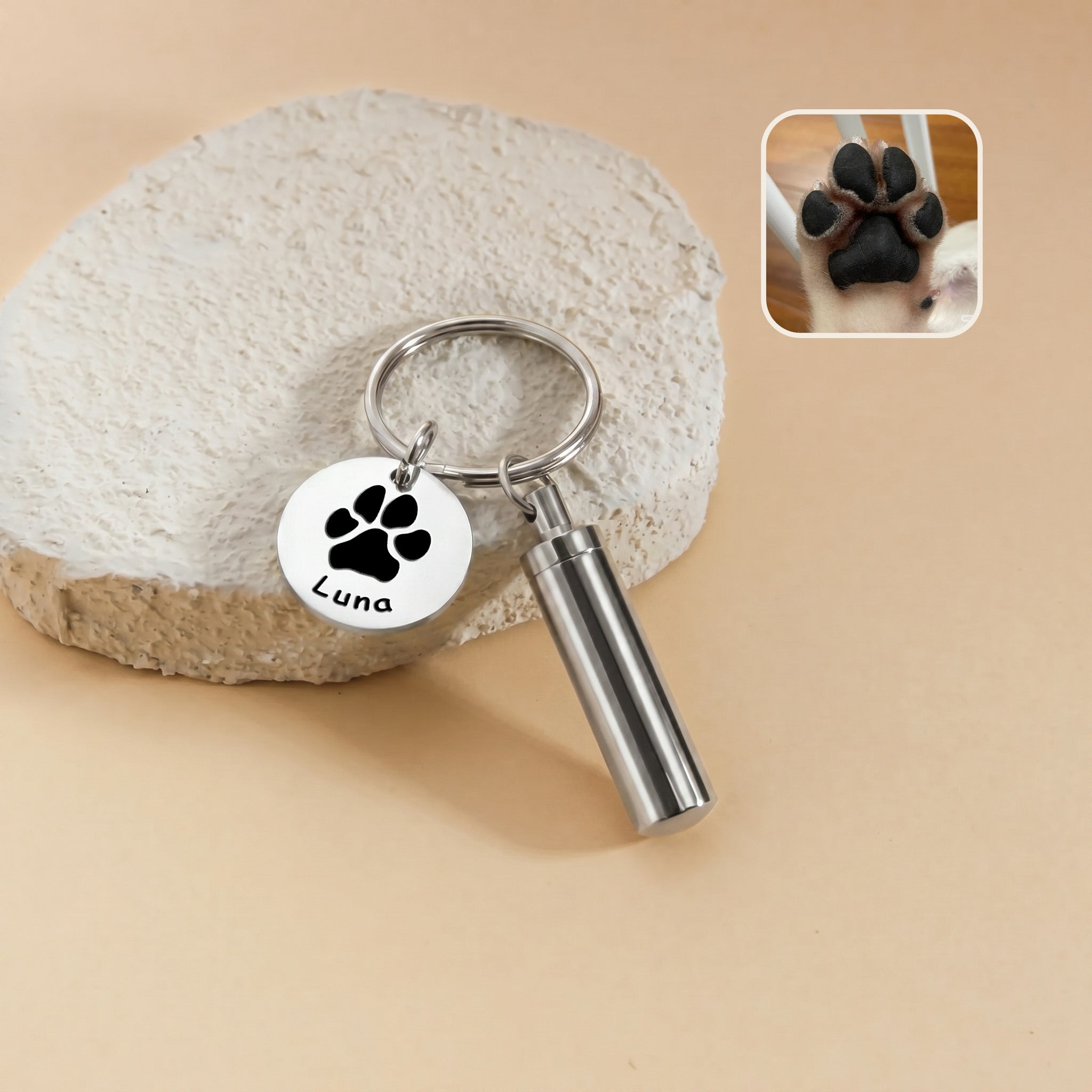 Rhodium-plated pet portrait and ashes cylinder keychain &mdash; engraved disc with a paw-print silhouette and the name Luna beside the cylinder urn, with a paw reference photo inset