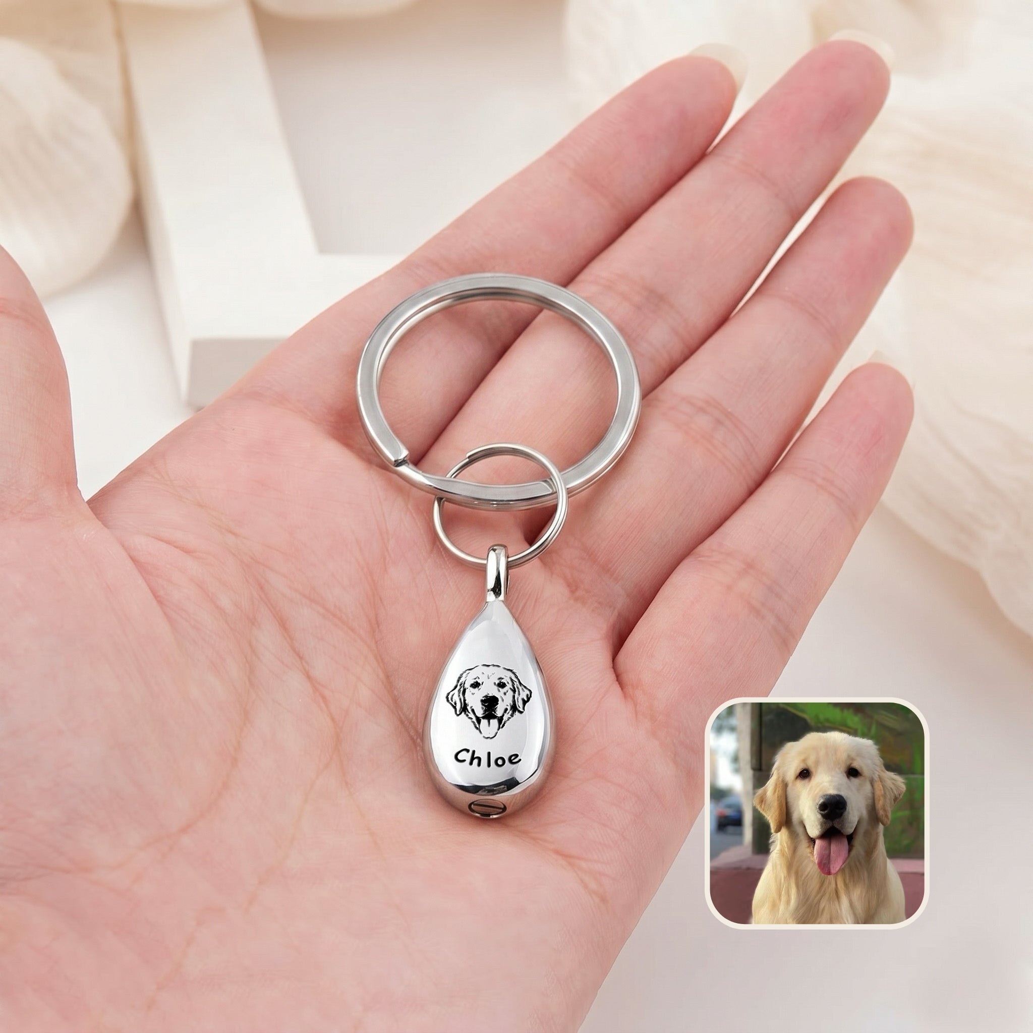 Rhodium-plated pet portrait ashes teardrop keychain held in an open hand for scale, with a dog reference photo inset