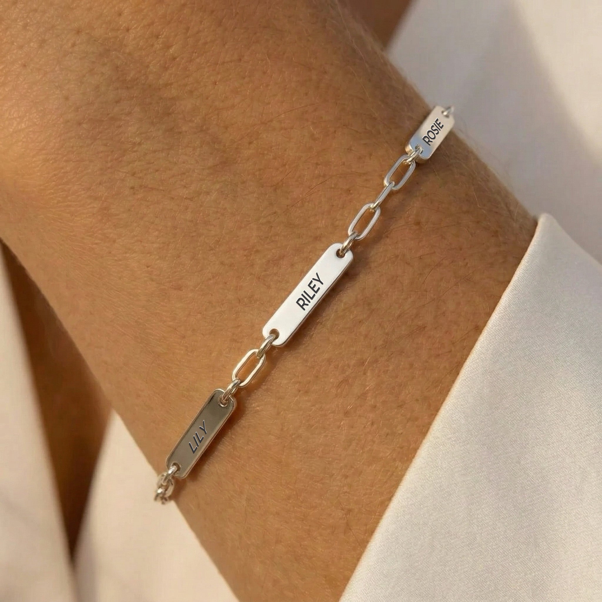 Silver rhodium paperclip chain pet name bracelet with three engraved name bars worn on a forearm