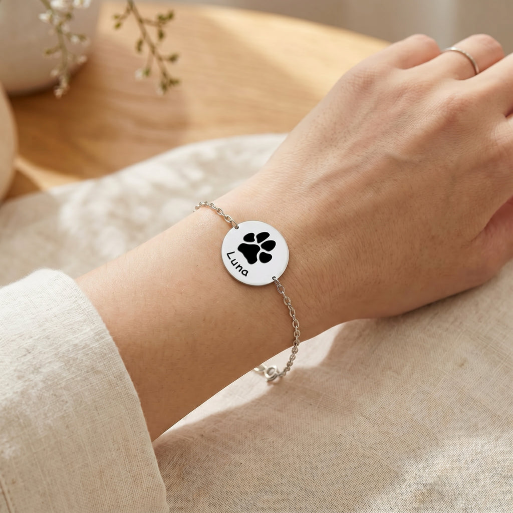 Rhodium chain bracelet on a wrist showing paw print engraving and name on disc charm, linen background