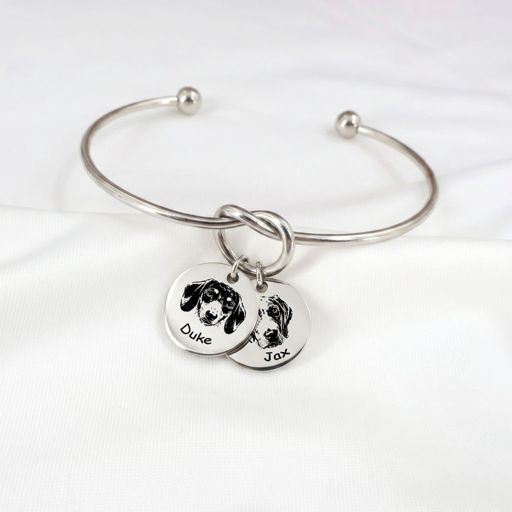 Silver rhodium knot cuff bracelet with two engraved pet portrait disc charms on a white background
