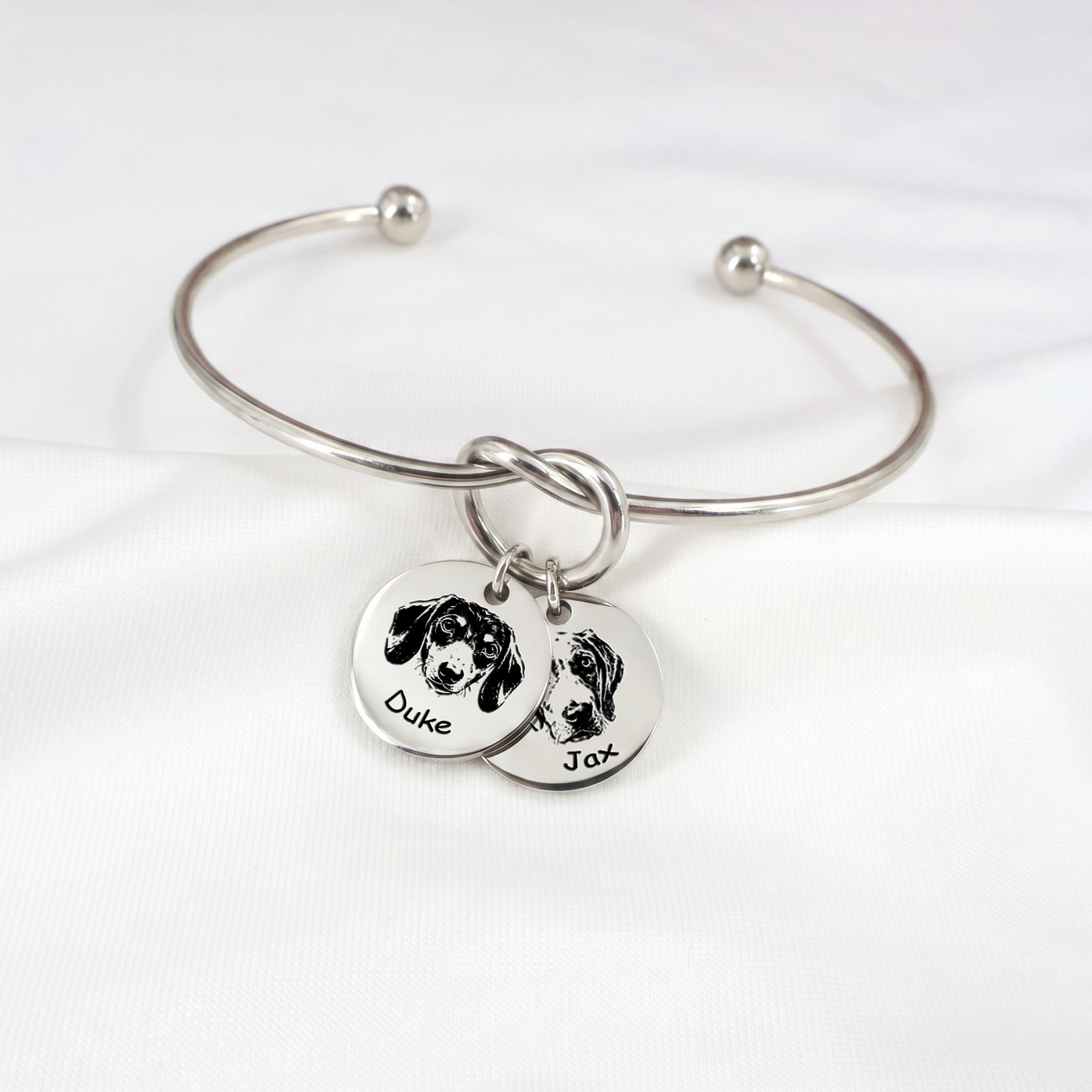 Silver rhodium knot cuff bracelet with two engraved pet portrait disc charms on a white background