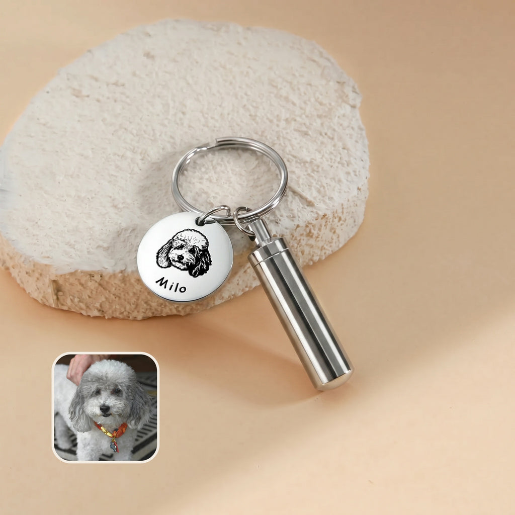 Rhodium-plated pet portrait and ashes cylinder keychain close-up &mdash; engraved disc with hand-drawn portrait and the name Milo beside the cylinder urn, with a reference photo inset