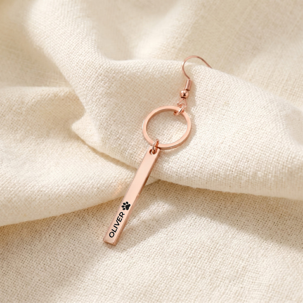 Close-up of a single rose gold pet name bar drop earring with an engraved name