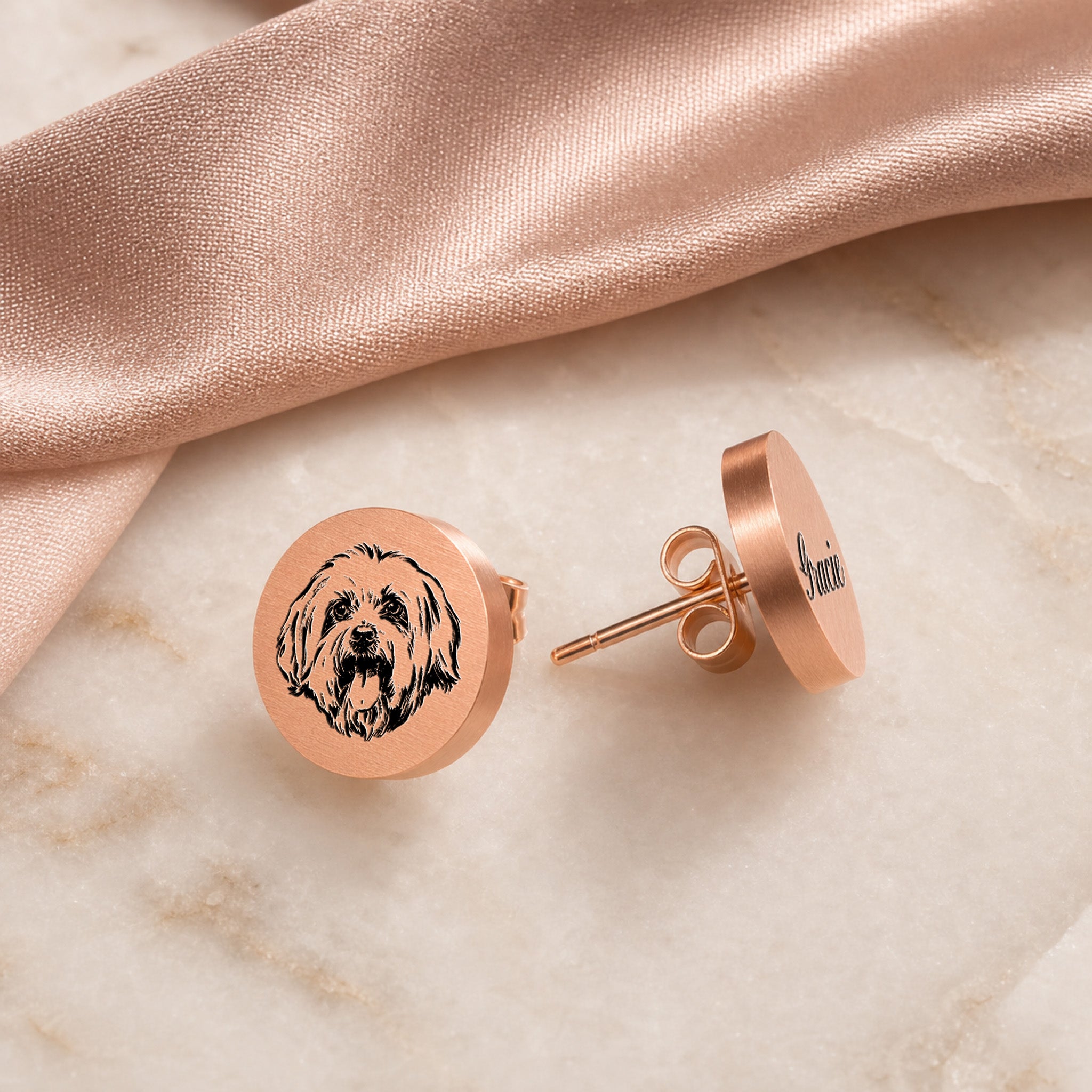Pair of rose gold pet portrait stud earrings on pale marble, portrait stud and engraved name stud side by side