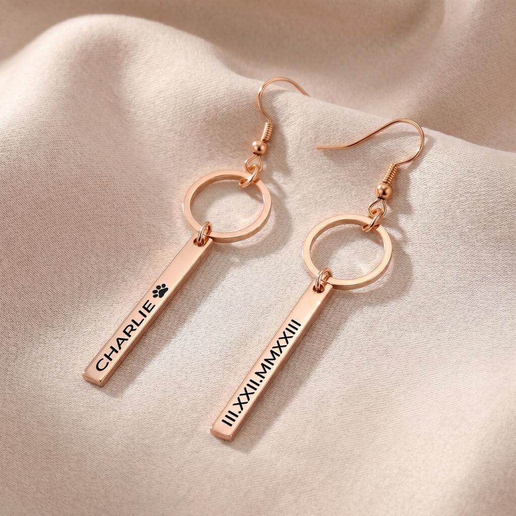 Pair of rose gold pet name bar drop earrings on warm neutral fabric