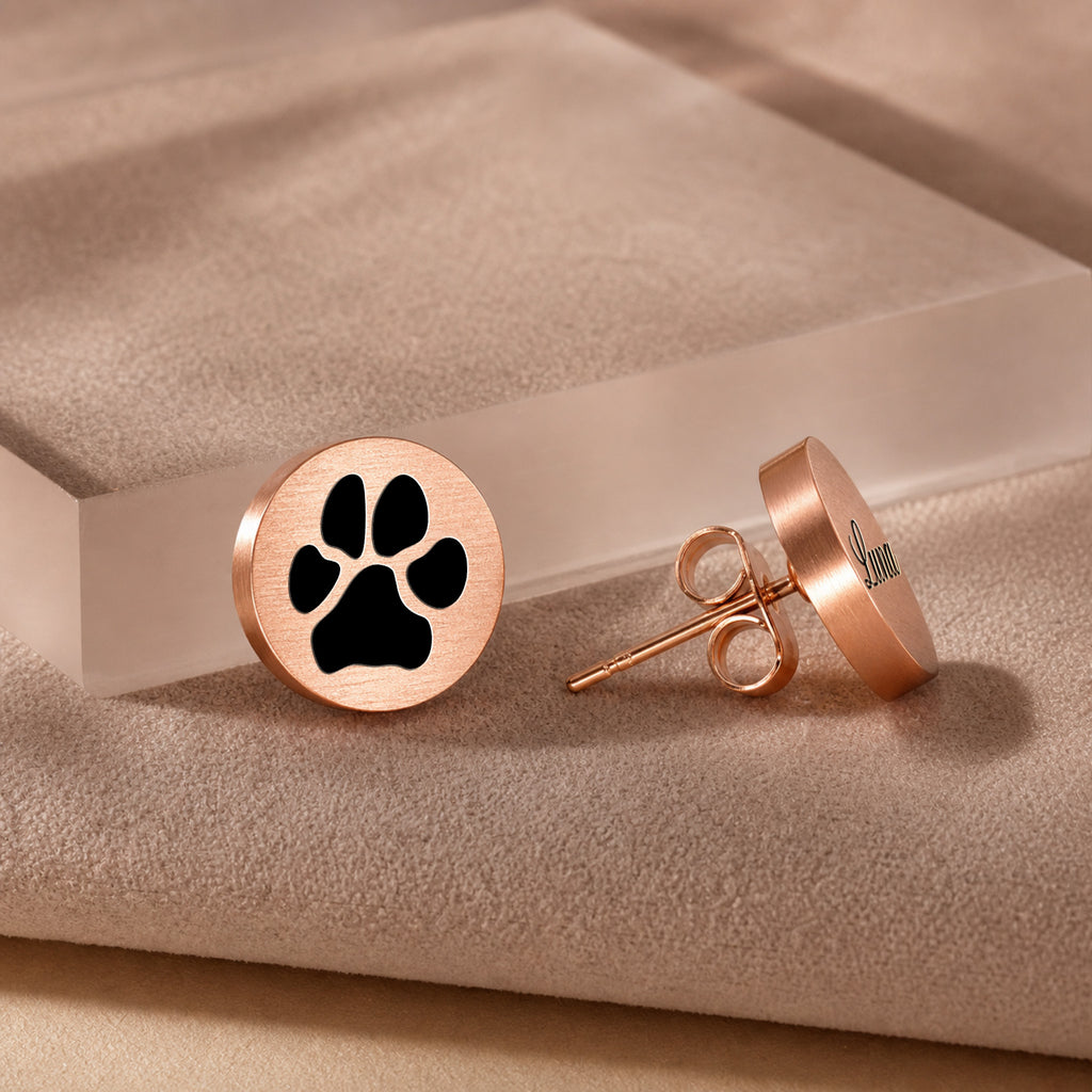 Rose gold pet name stud earring with script-engraved pet name on a round disc, on a beige textured block