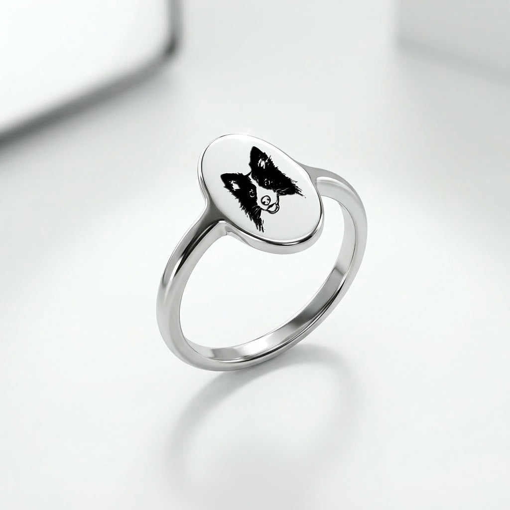 Silver rhodium oval signet ring at a three-quarter angle, hand-drawn pet portrait on the oval face, slim band, soft reflective surface