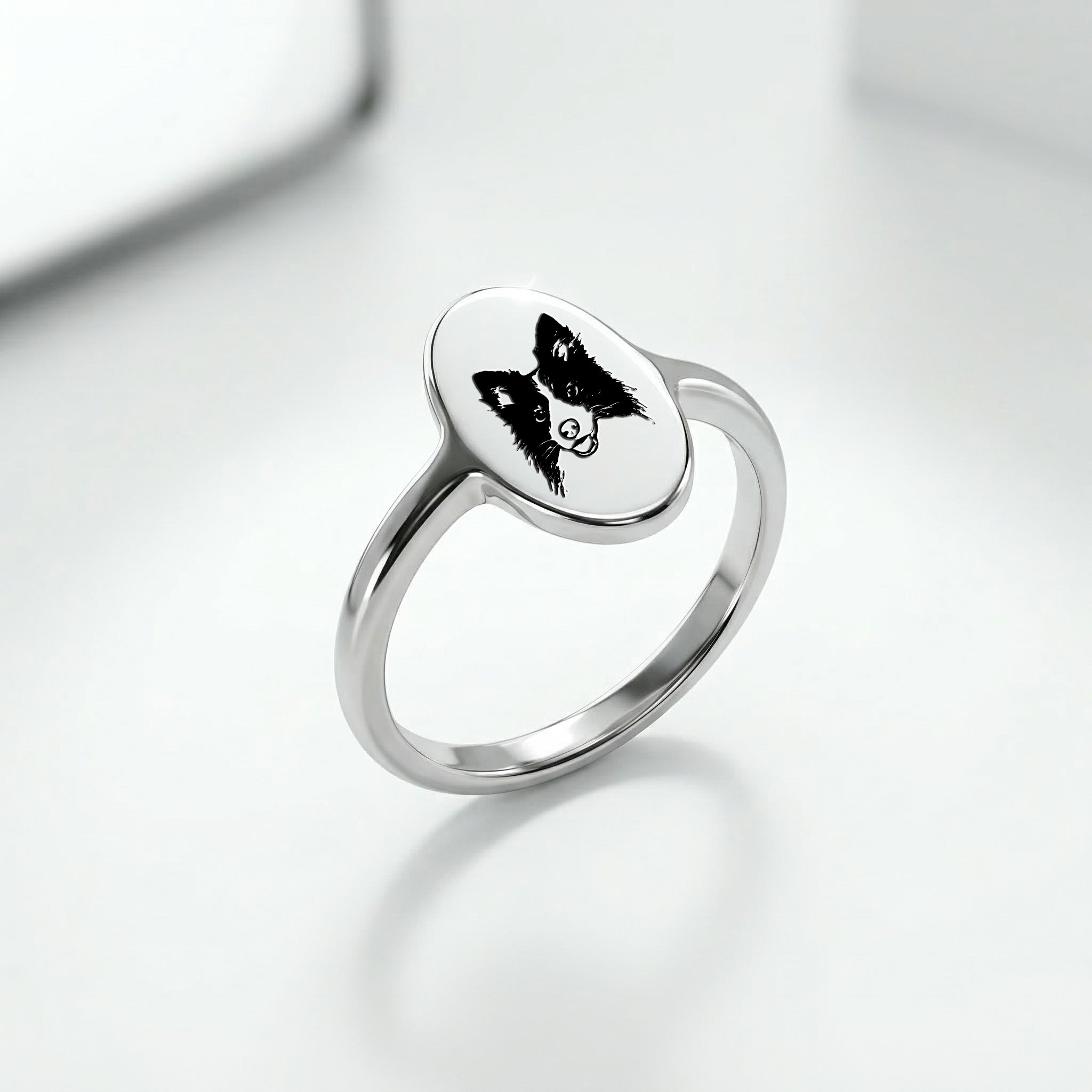 Silver rhodium oval signet ring at a three-quarter angle, hand-drawn pet portrait on the oval face, slim band, soft reflective surface