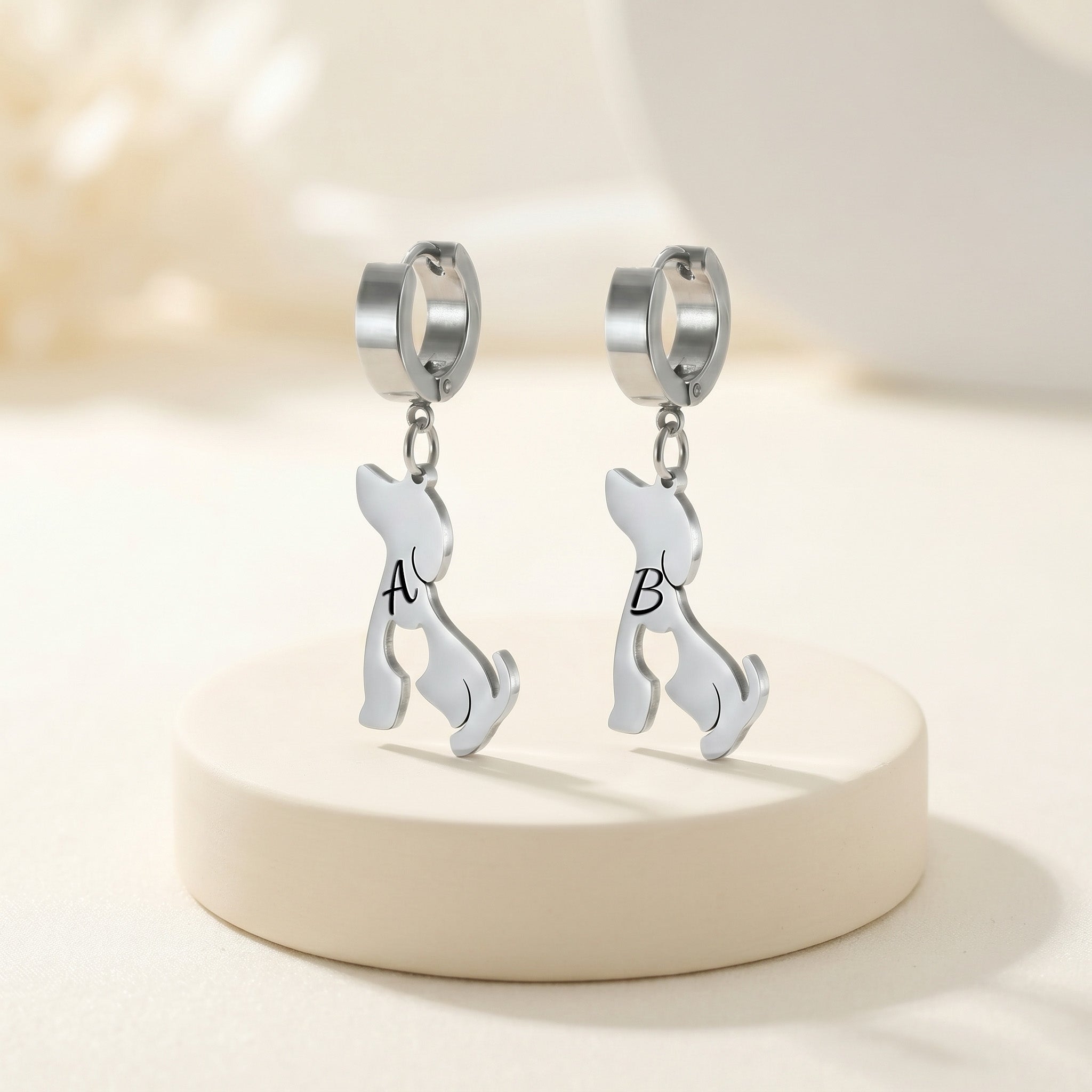 Pair of silver dog-silhouette name earrings on a white pedestal