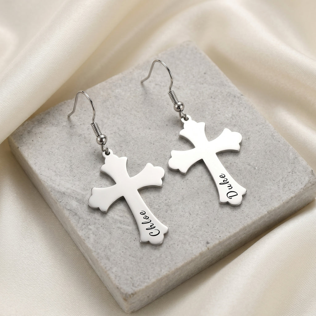 Rhodium silver pet cross earrings, the pair displayed on a pale stone tile — script pet-name engraving visible on each cross