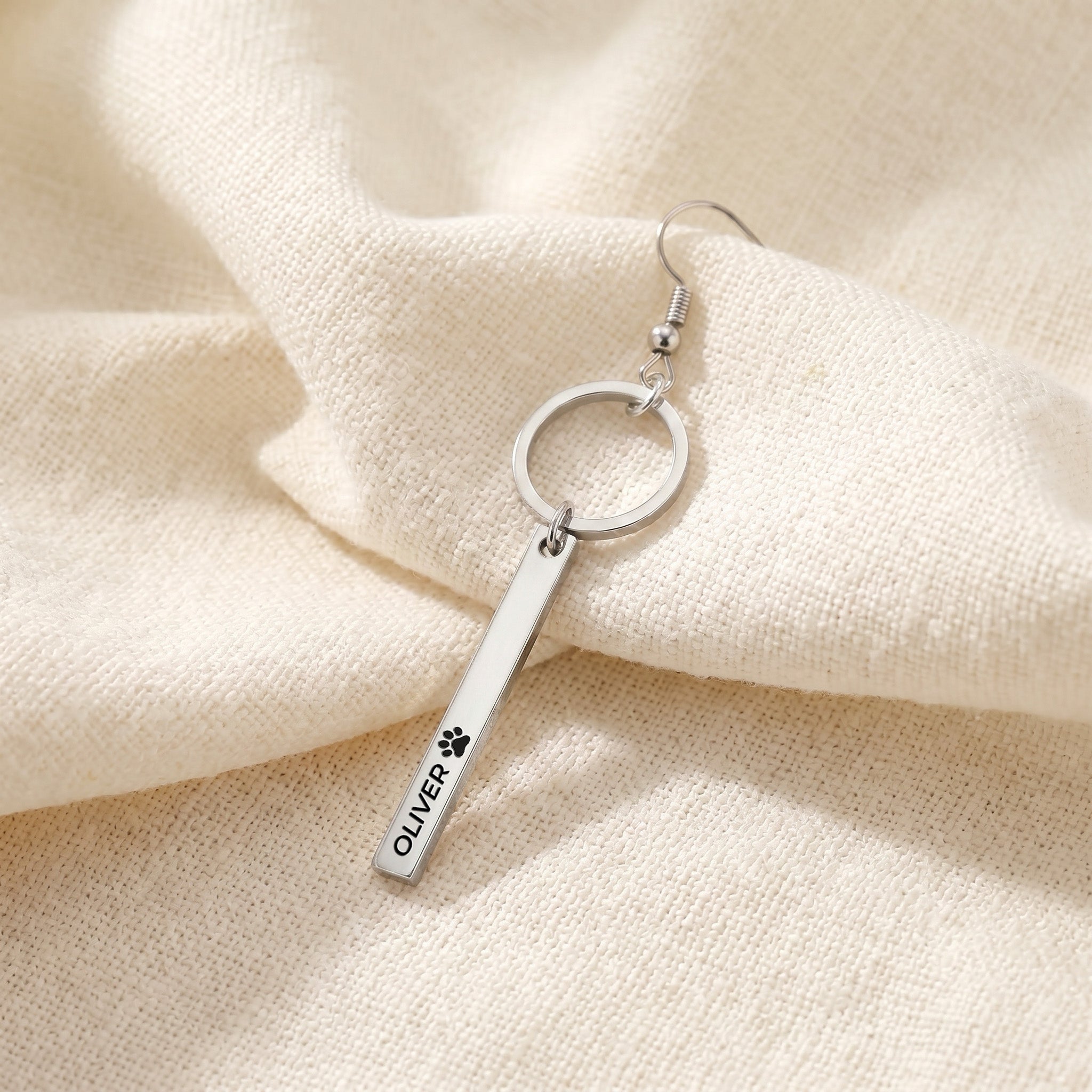 Close-up of a single silver pet name bar drop earring with an engraved name