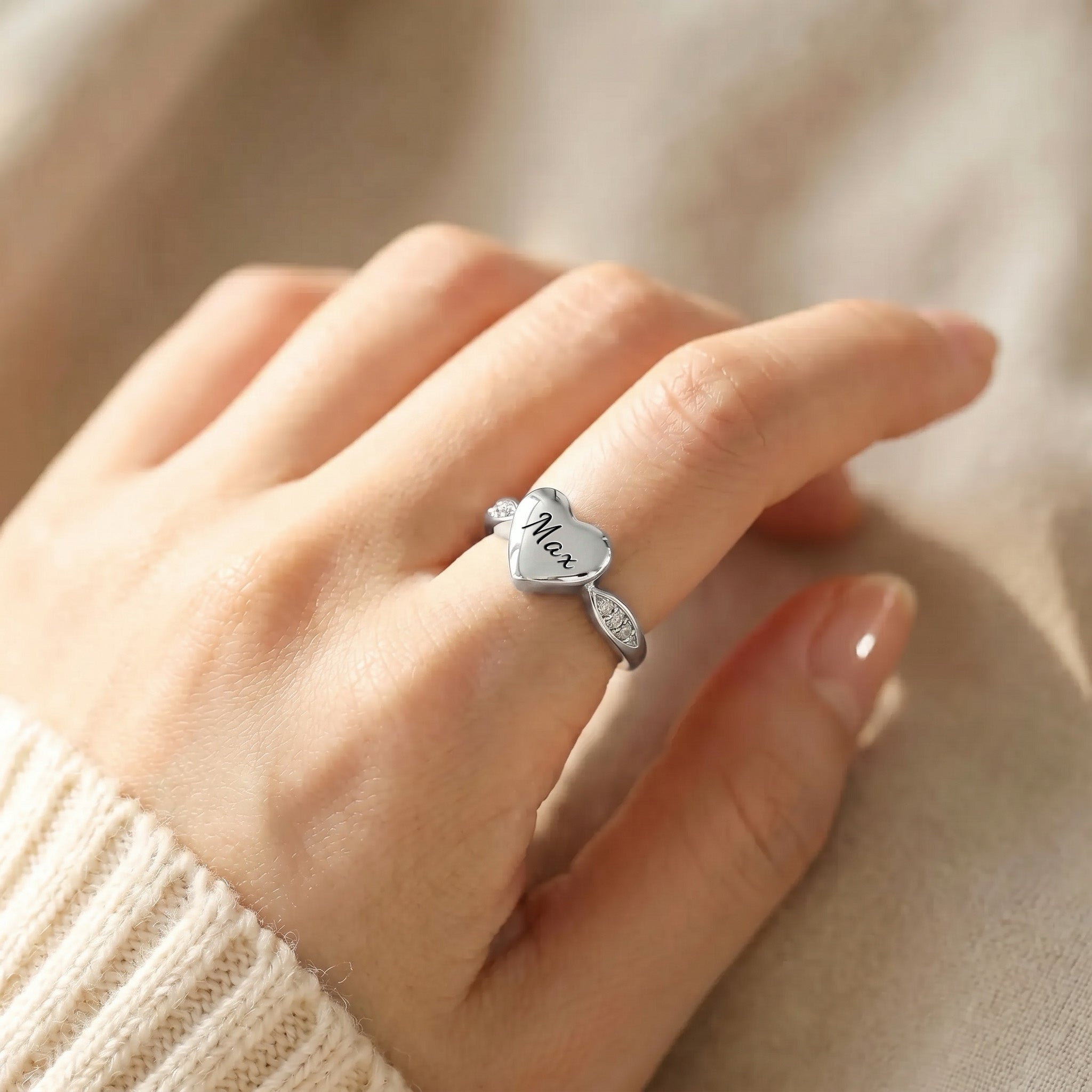 Silver heart urn ring worn on a hand, name visible on the heart face, sweater sleeve background