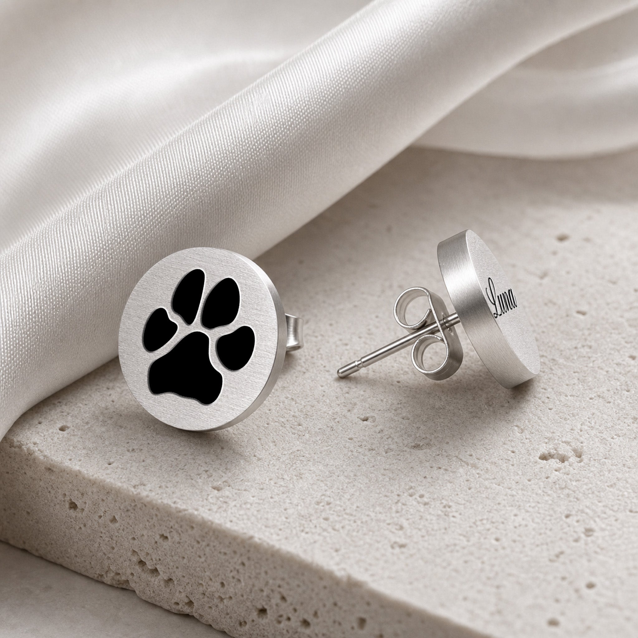 Silver pet name stud earring with script-engraved pet name on a round disc, staged on light stone