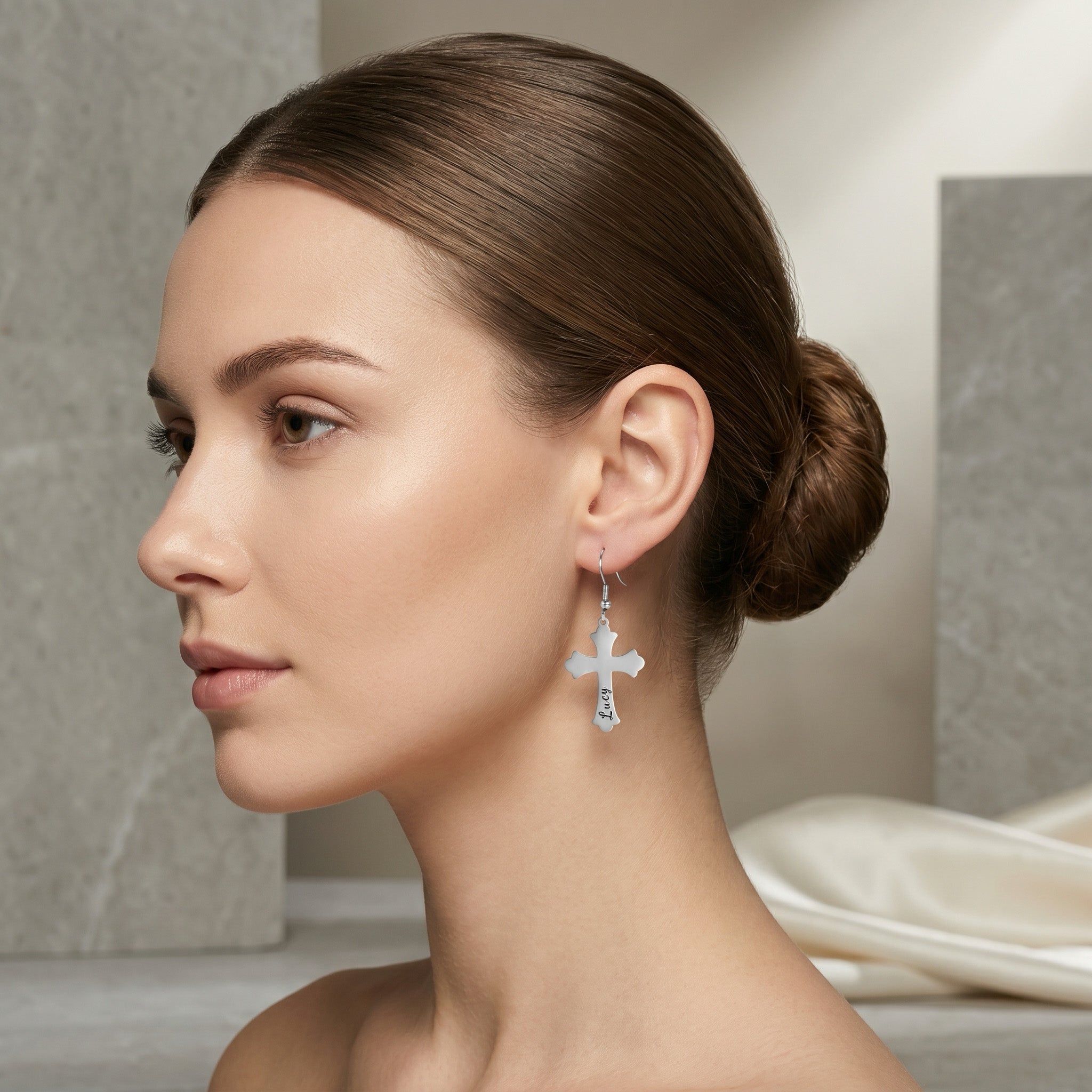 Model in side profile wearing a single rhodium silver pet cross drop earring engraved with a pet name in script, in a neutral studio scene