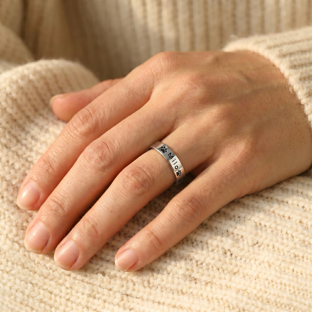 Rhodium-plated pet name stacking ring worn on a hand resting on a cream knit sweater
