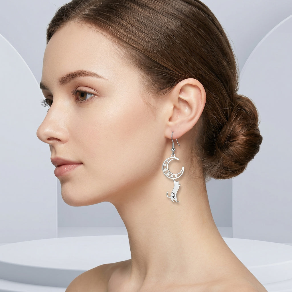 Silver cat-and-moon name drop earring worn in profile with hair in a bun against pale studio arches