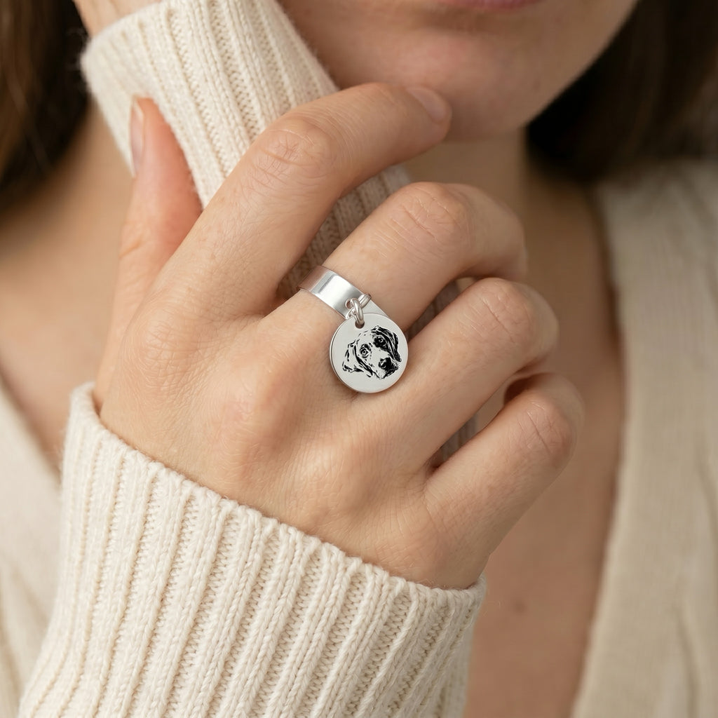 Silver-tone pet portrait disc ring on a finger, with a cream knit sleeve in a soft indoor crop