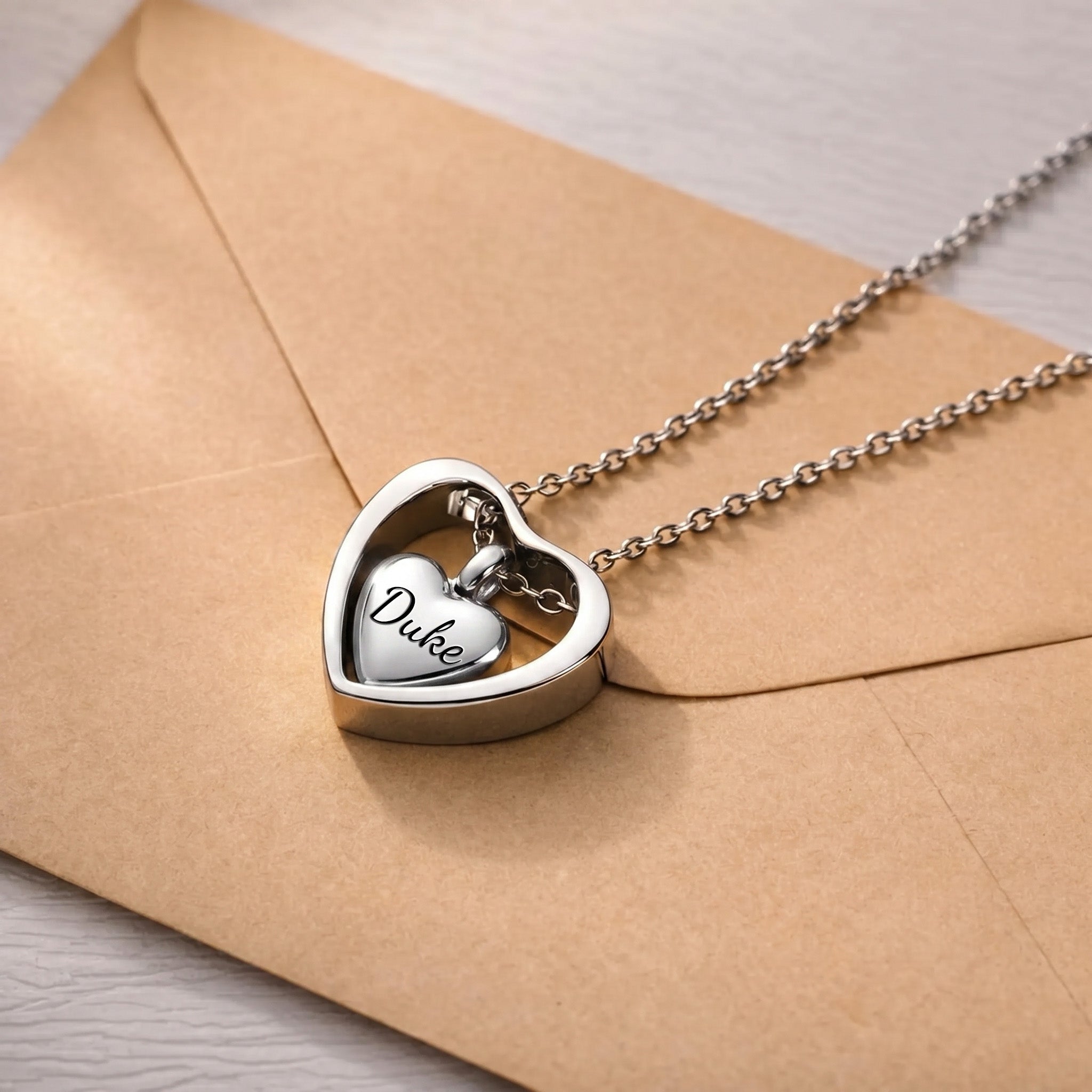 Rhodium heart urn cremation necklace on kraft envelope, name engraved on inner heart pendant