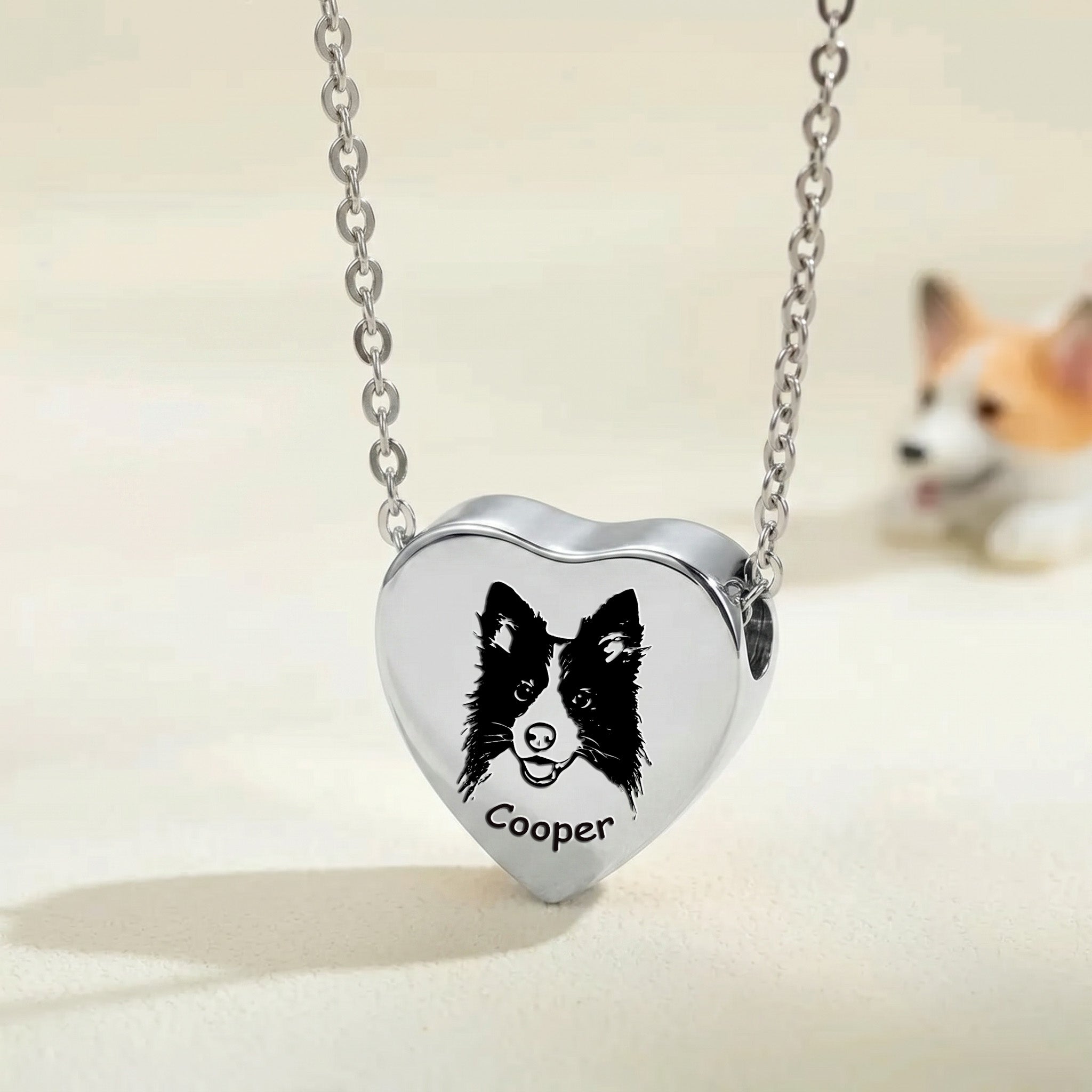 Rhodium pet photo heart urn necklace close-up showing hand-drawn portrait engraving with blurred corgi in background