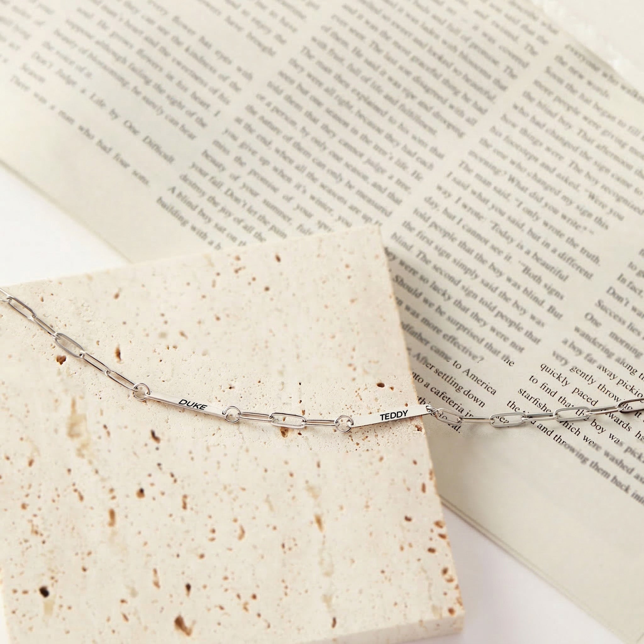 Silver paperclip chain pet name necklace with two engraved name bars on travertine stone, product view