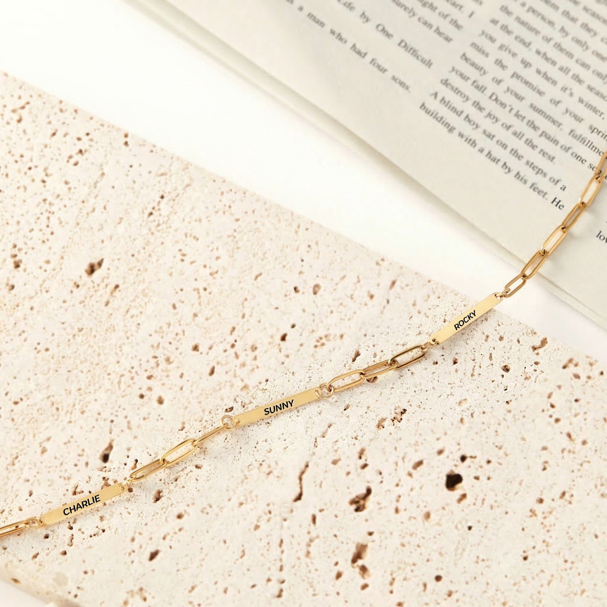 Gold paperclip chain pet name necklace with three engraved name bars on travertine stone, product view