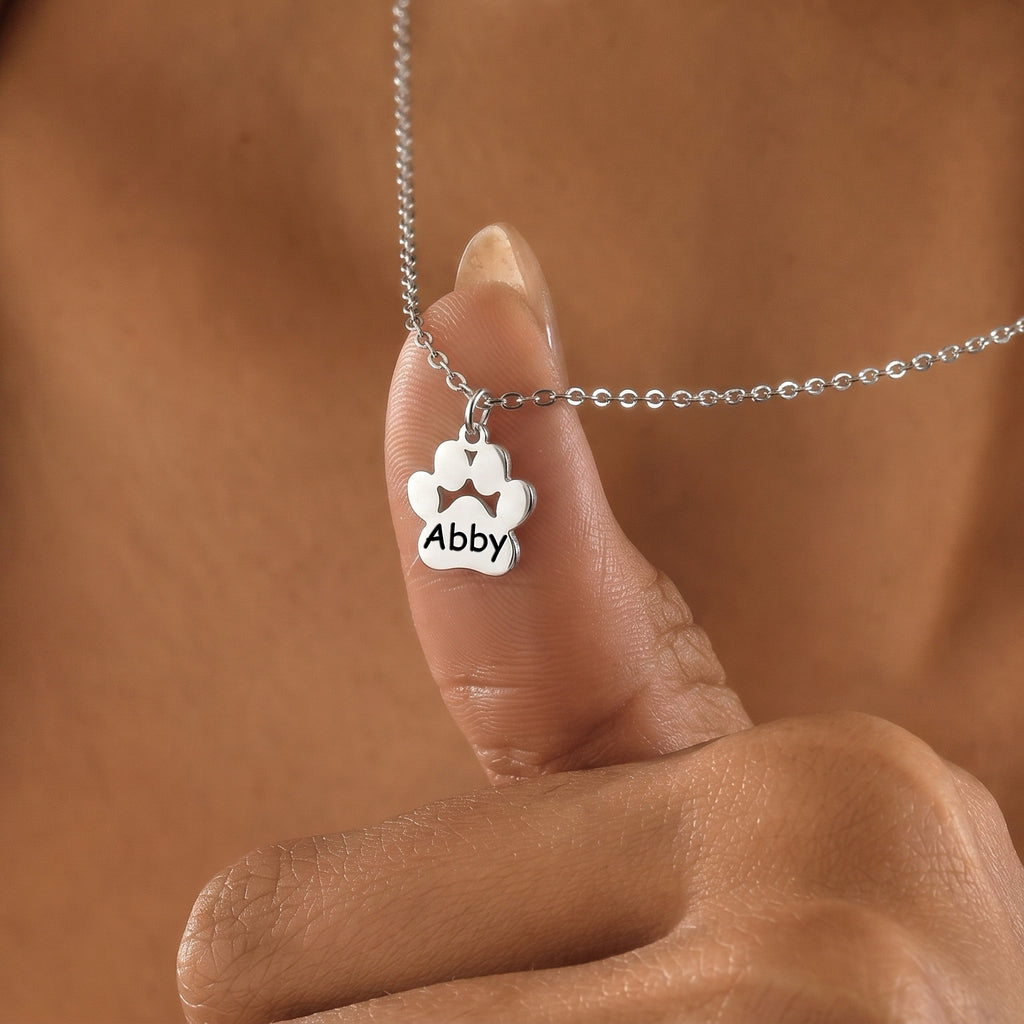 Silver rhodium paw print pendant engraved with name Abby held between fingers