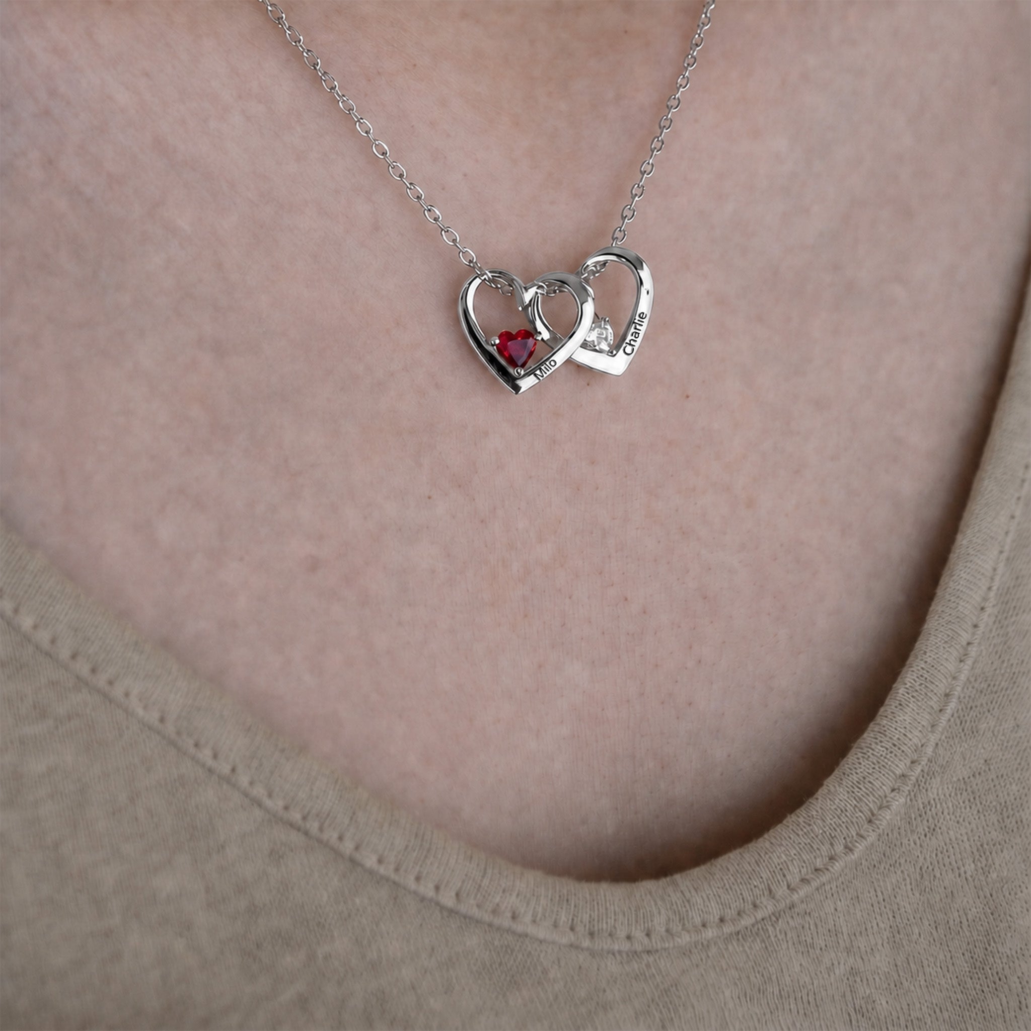 Rhodium-plated heart birthstone necklace worn, two hearts with engraved names and red and clear birthstones