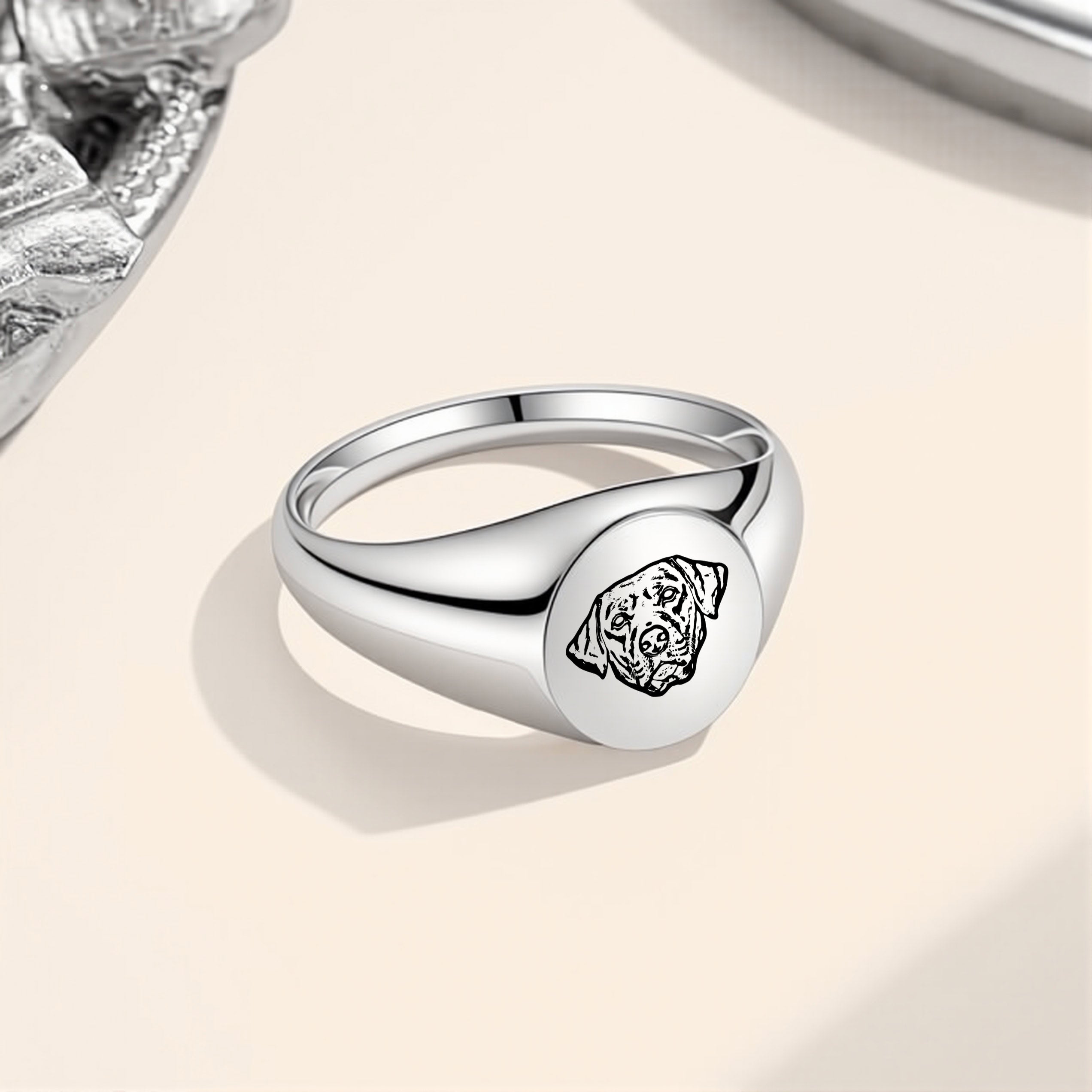 Silver pet portrait signet ring with engraved portrait placed on a beige surface
