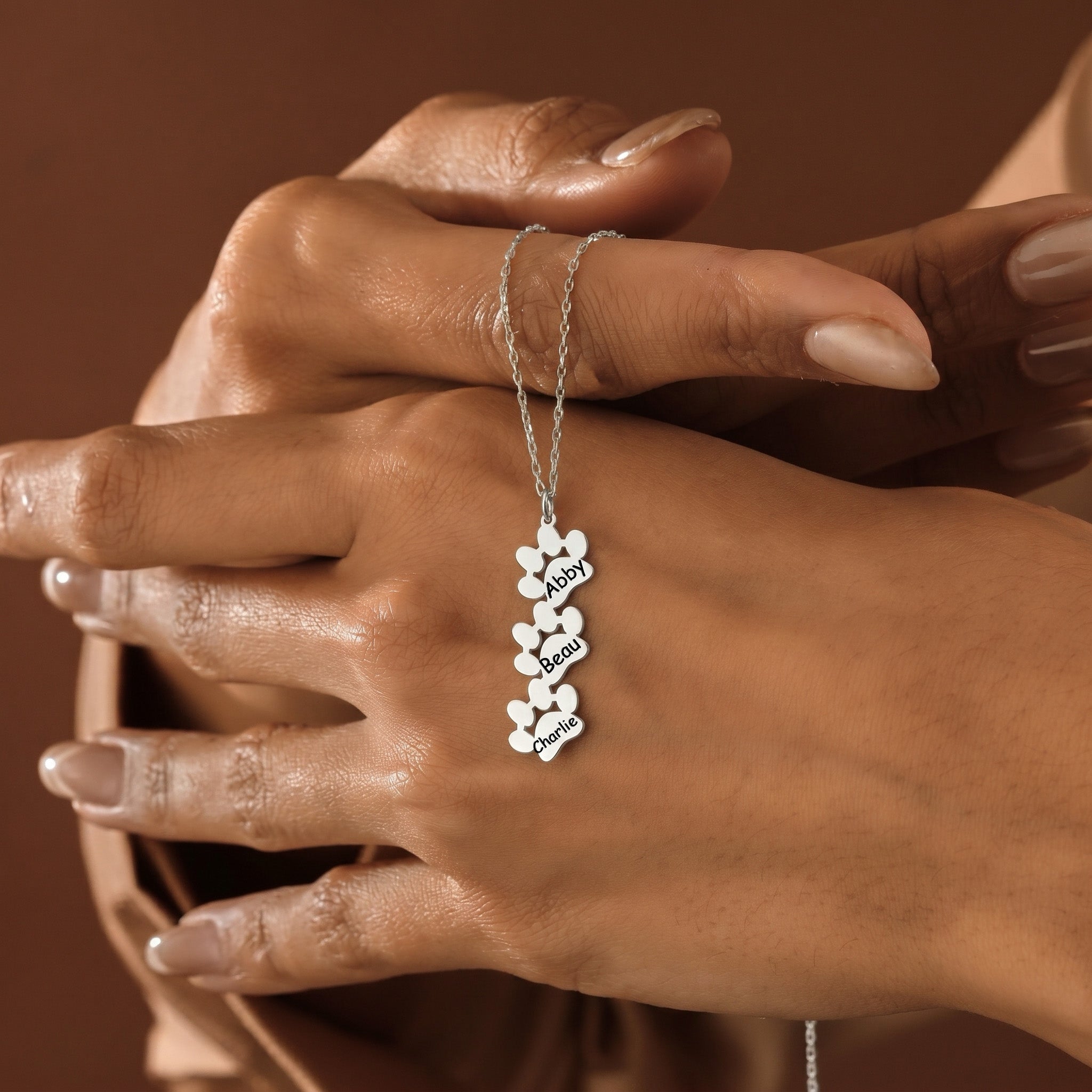 Three silver paw print pendants with engraved names held against hand