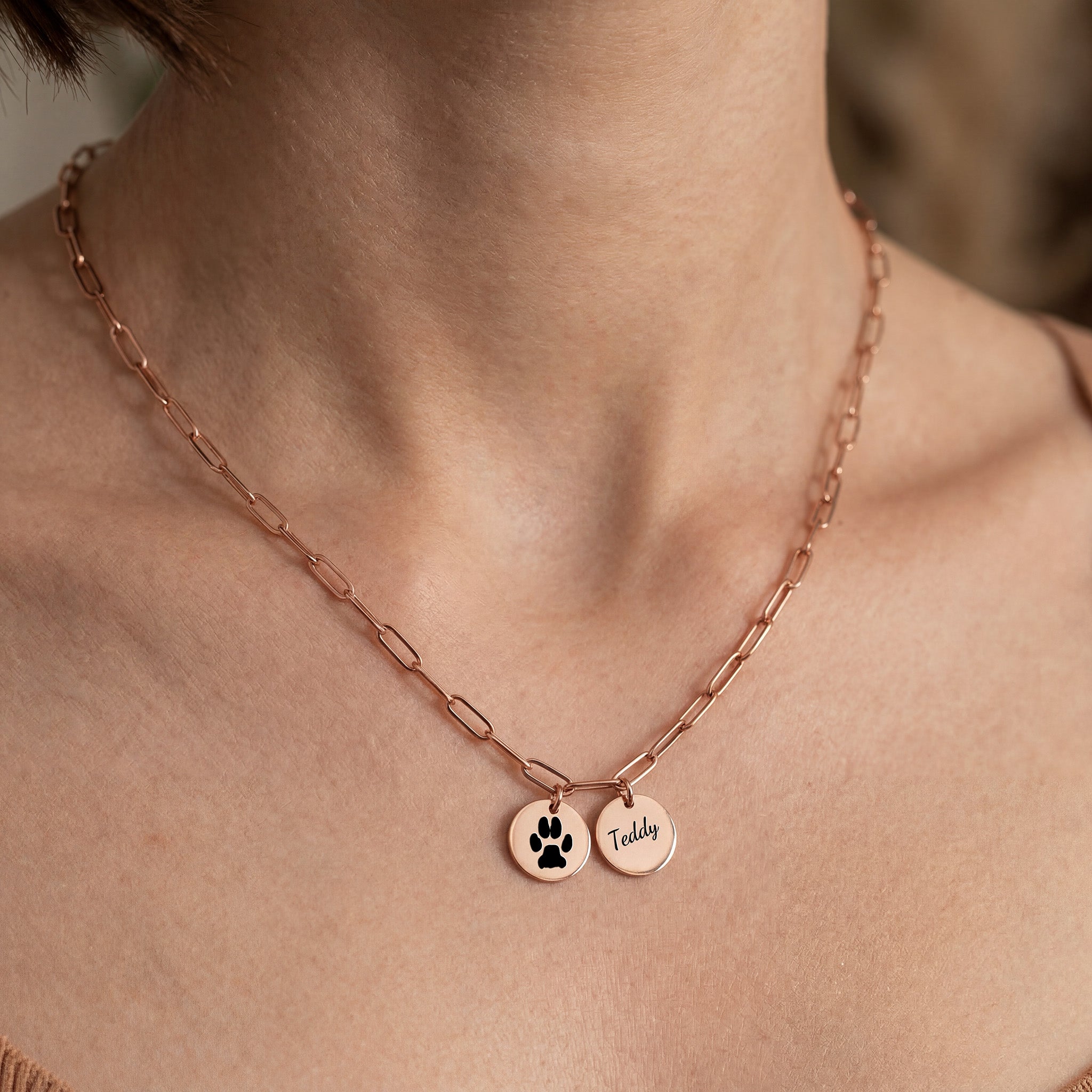 Woman wearing rose gold paperclip chain necklace with paw print and name pendants