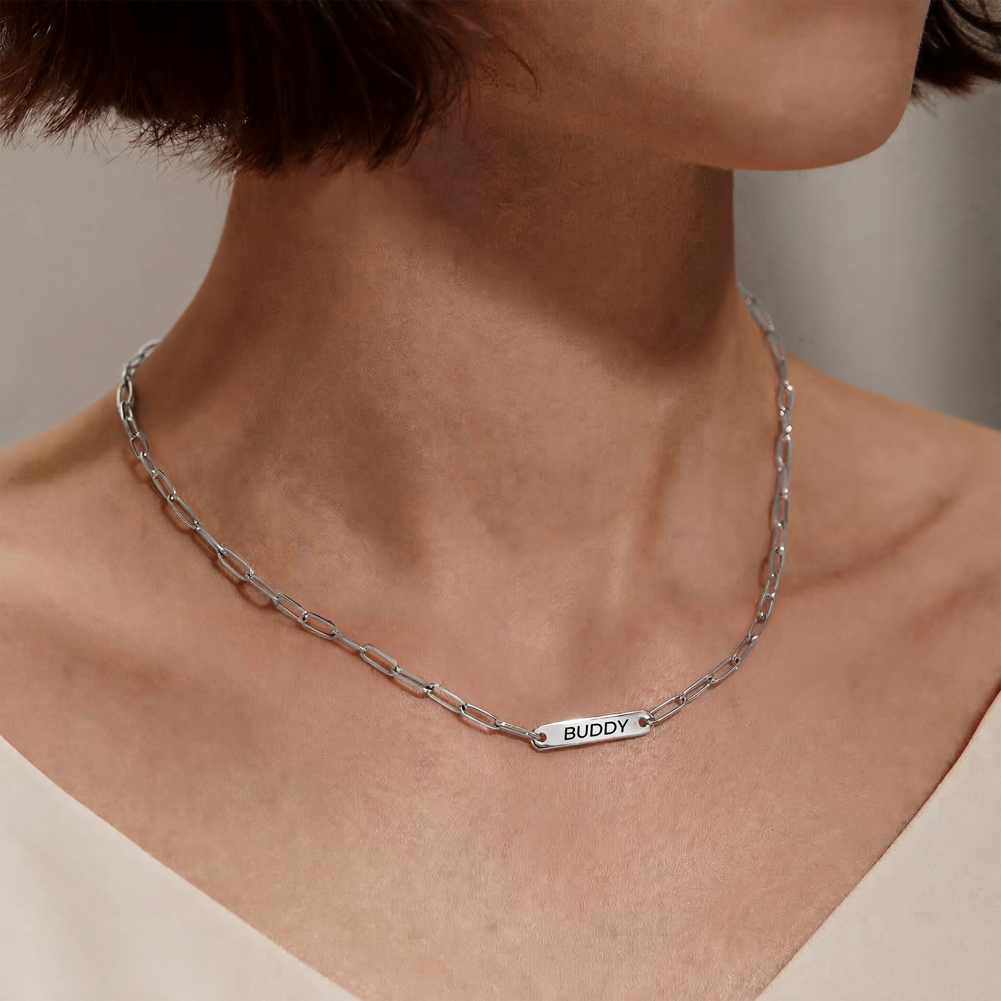 Woman wearing silver paperclip chain pet name necklace with one engraved name bar