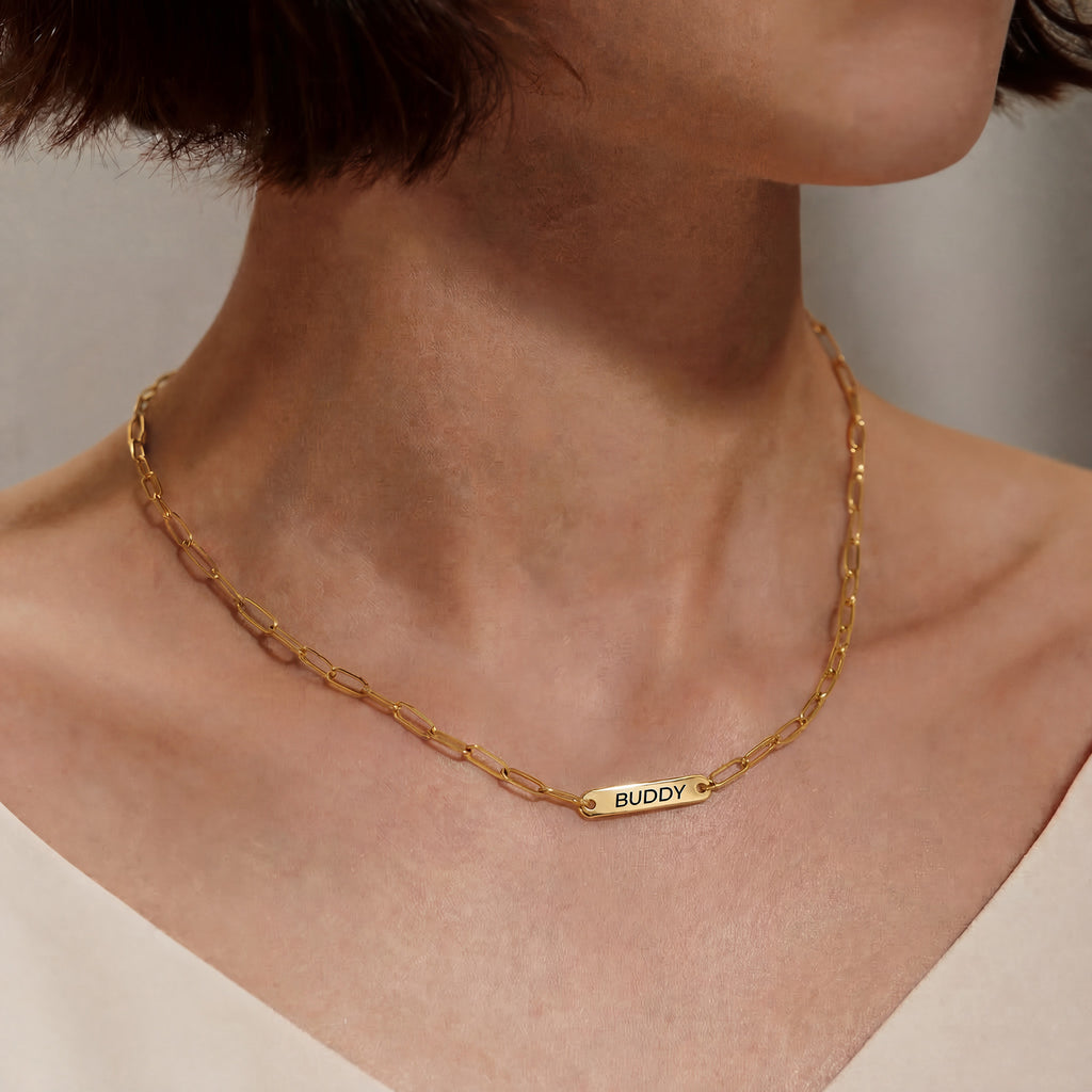 Woman wearing gold paperclip chain pet name necklace with single engraved name bar at the collarbone