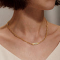 Woman wearing gold paperclip chain pet name necklace with single engraved name bar at the collarbone