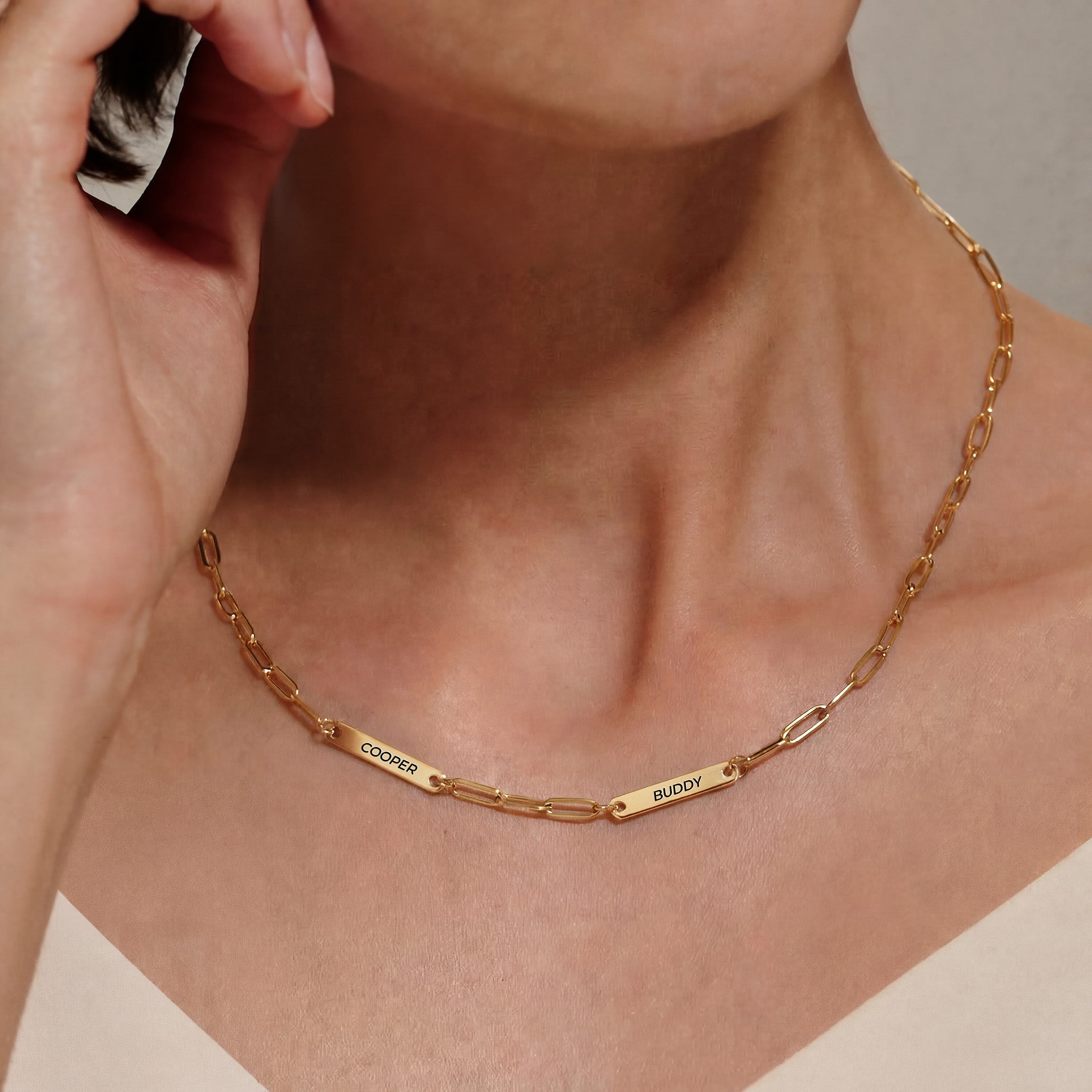 Woman wearing gold paperclip chain pet name necklace with two engraved pet name bars on her neckline