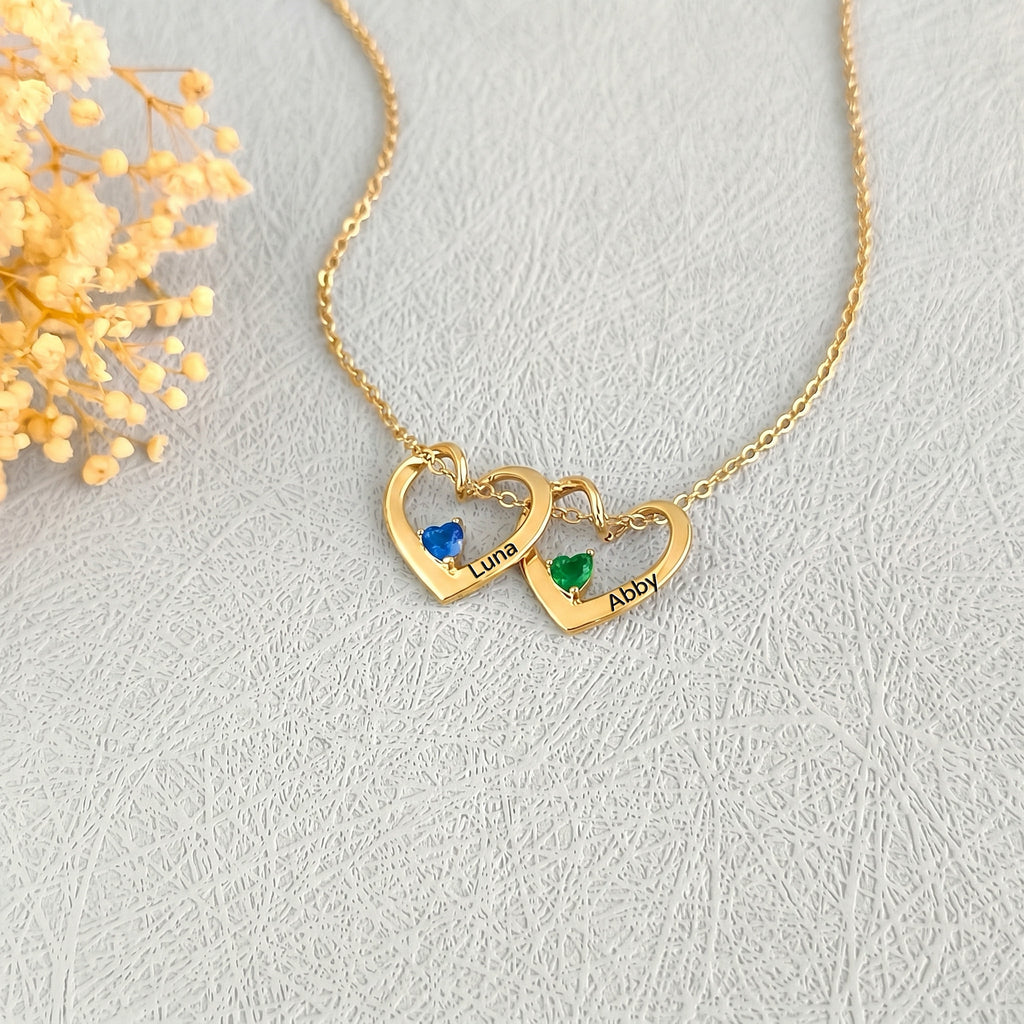 Two 18K gold heart pendants with blue and green birthstones and engraved pet names Luna and Abby
