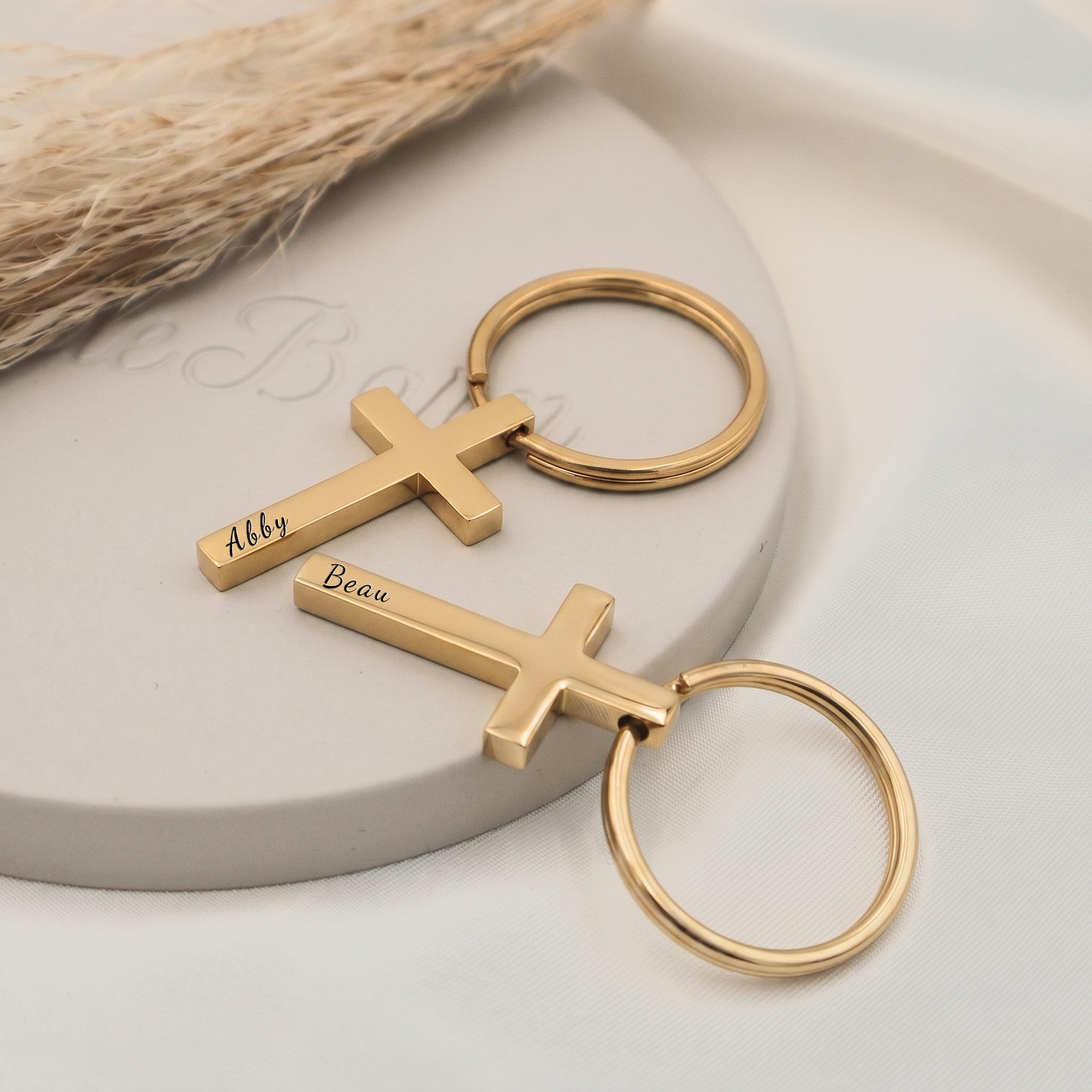 18k yellow gold pet cross keychain shown as a pair staged on a ceramic tray — hand-drawn portrait + script name engraved on each cross pendant front