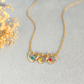 Three gold heart pendants with colorful birthstones and pet names on cream background