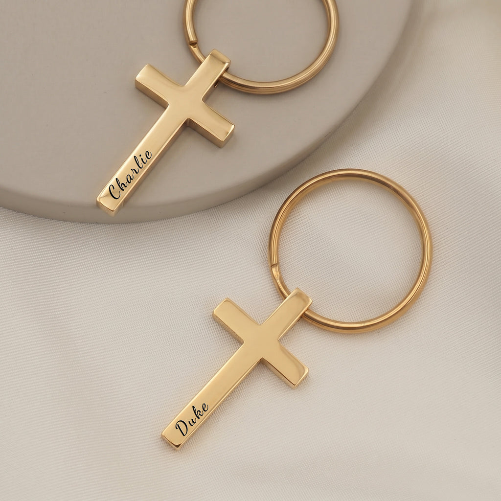 18k yellow gold pet cross keychain pair on ceramic tray with soft white fabric — front-face hand-drawn portrait + pet name engraving visible