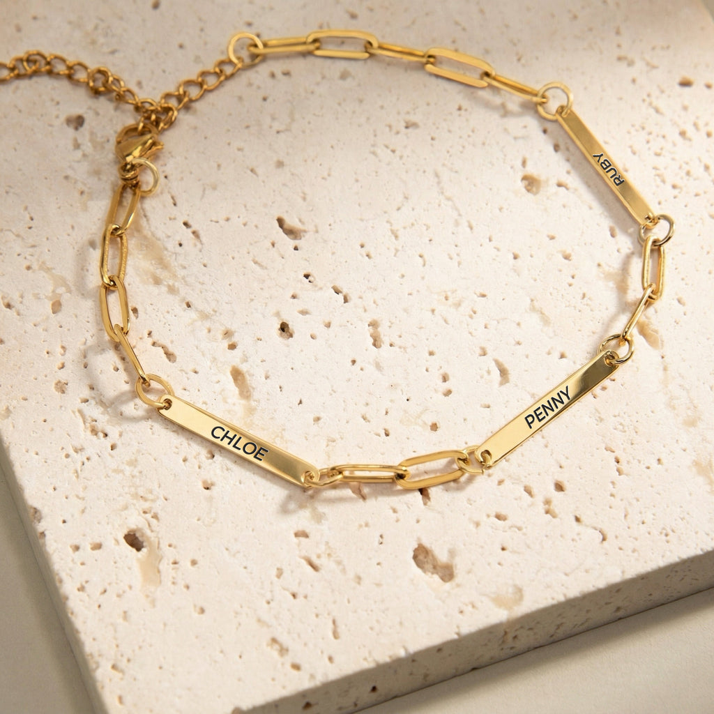 Gold paperclip chain pet name bracelet with three engraved name bars on a cream stone block