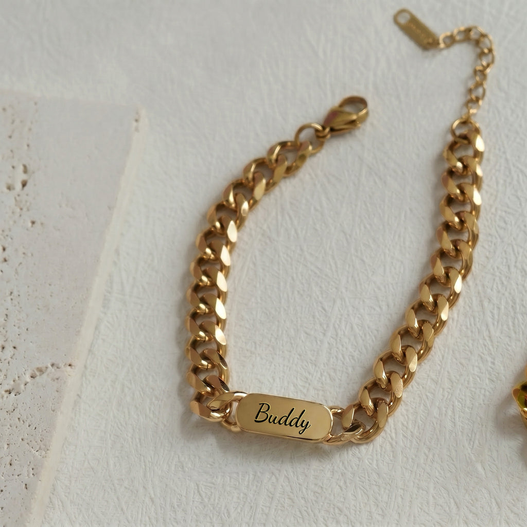 18K gold pet name bracelet laid flat, a name engraved in script on the oval plate