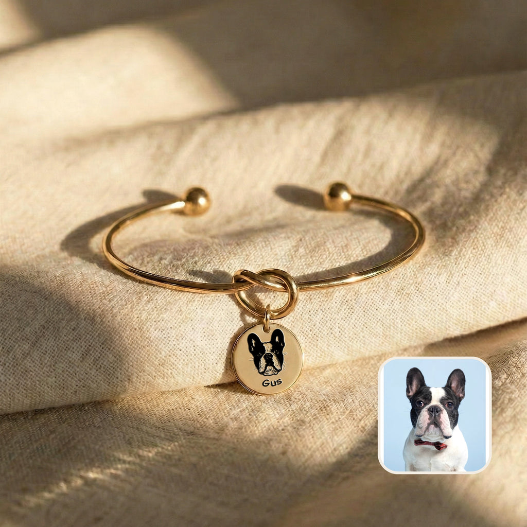 Gold knot cuff bracelet with engraved French bulldog portrait disc charm on cream fabric, beside the source pet photo