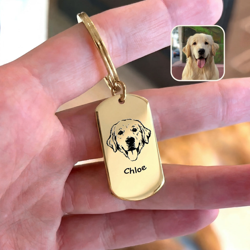 18K gold pet portrait dog tag keychain held in hand beside original dog reference photo, warm indoor styled scene