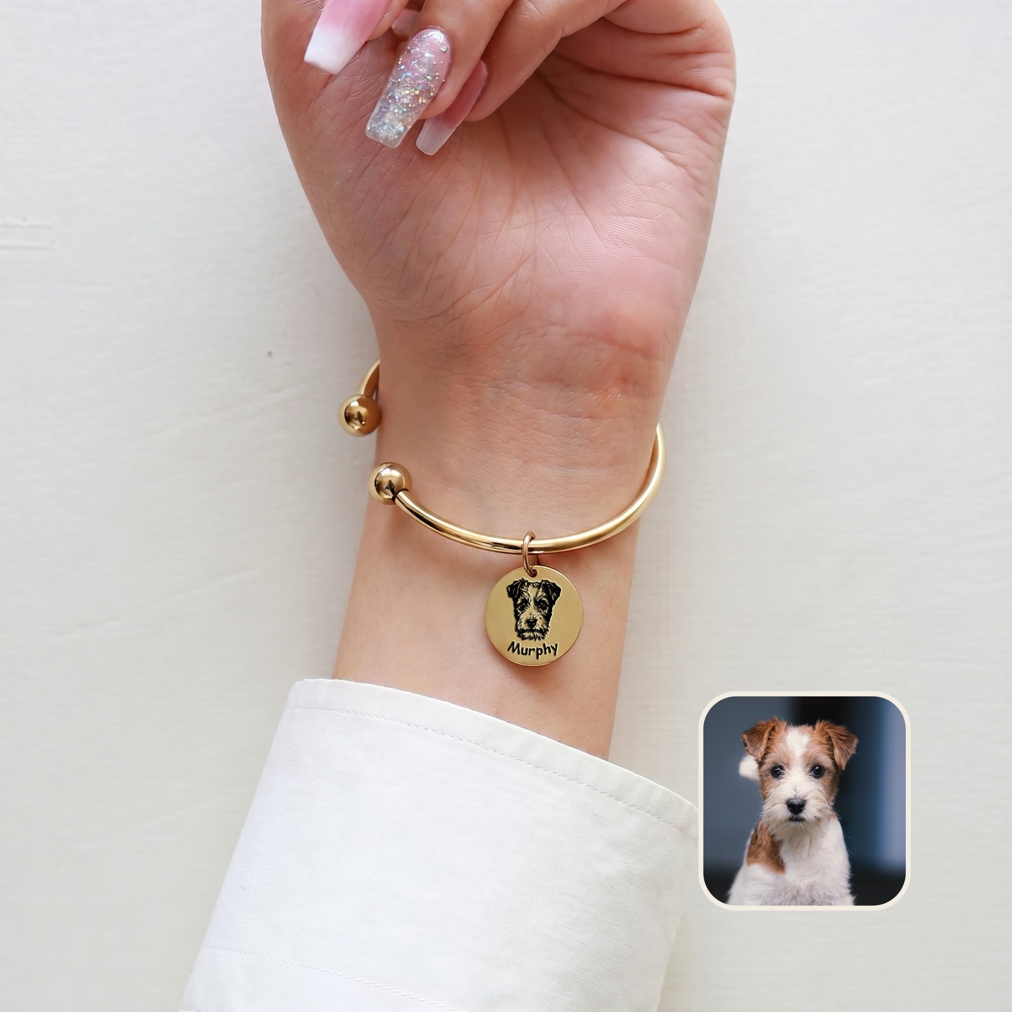 Gold-plated pet portrait cuff bracelet on a wrist against a plain wall, with an inset terrier reference photo