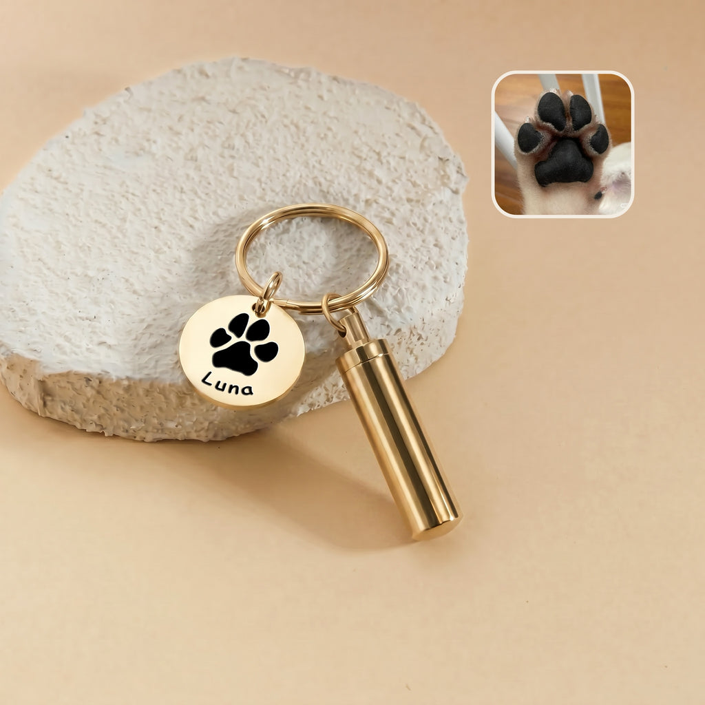 18k gold-plated pet portrait and ashes cylinder keychain &mdash; engraved disc with a paw-print silhouette and the name Luna beside the cylinder urn, with a paw reference photo inset
