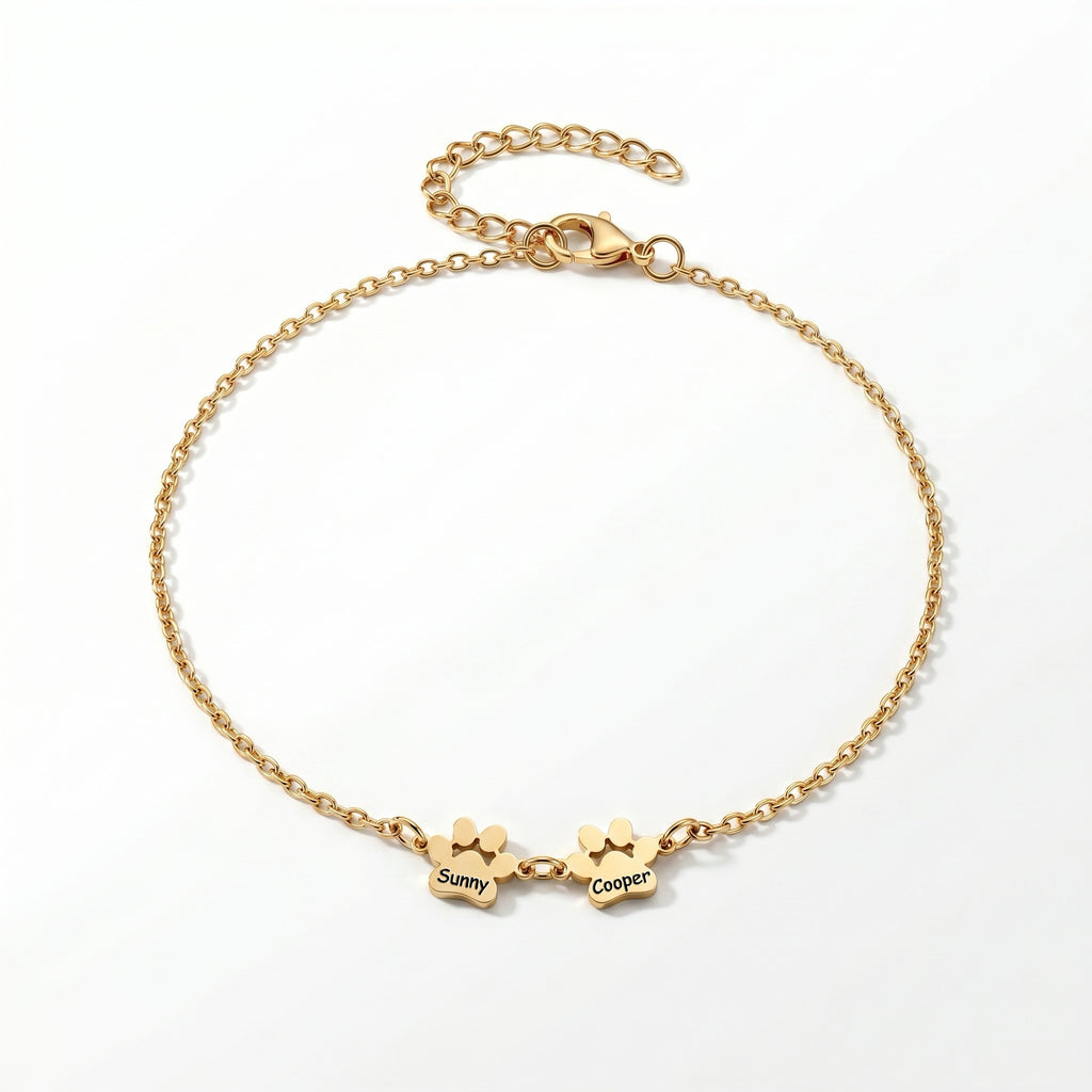 Gold paw print name bracelet with two engraved charms on a plain white background