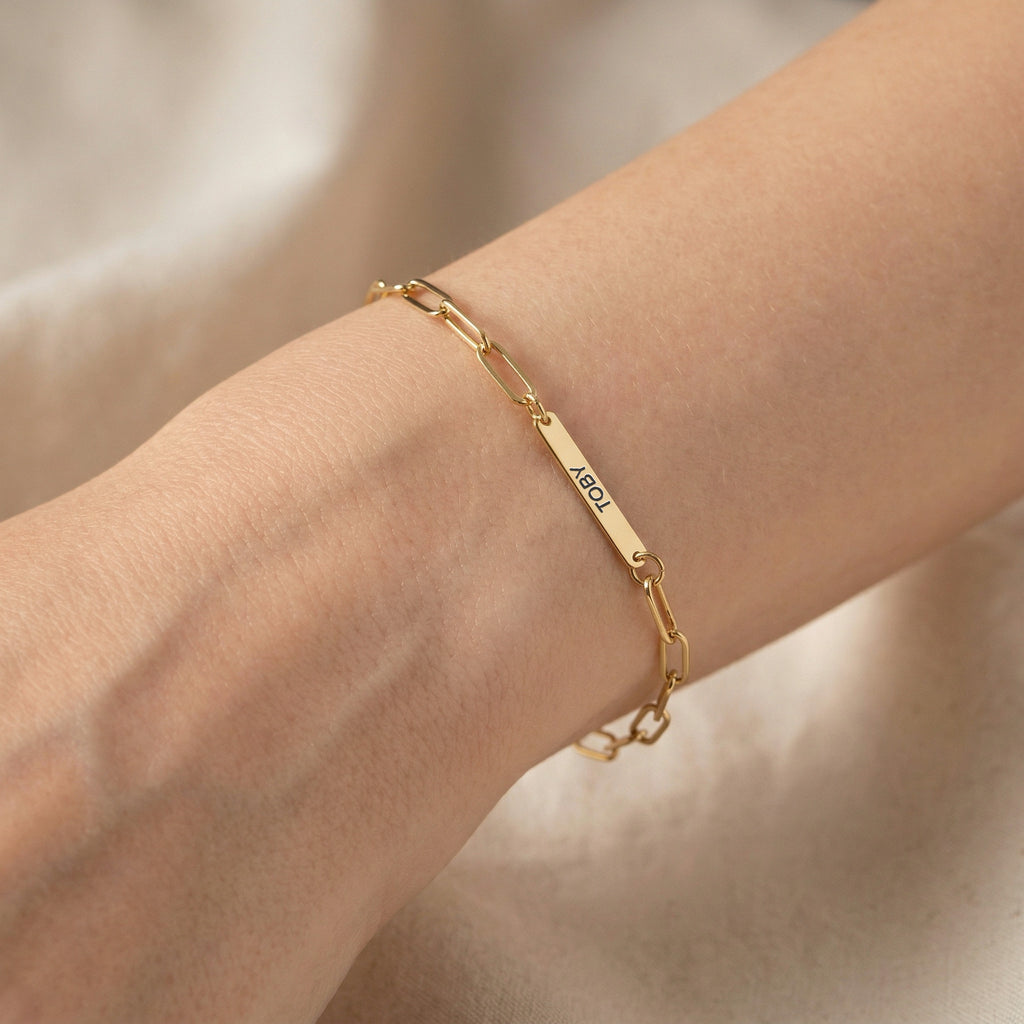 Gold paperclip chain pet name bracelet with a single engraved name bar worn on a wrist