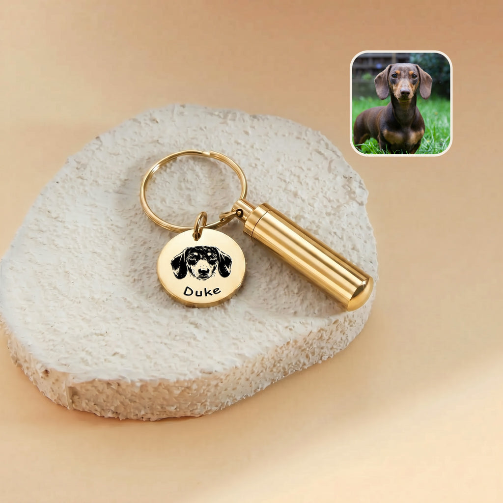 18k gold-plated pet portrait and ashes cylinder keychain close-up &mdash; engraved disc with hand-drawn dachshund portrait and the name Duke beside the cylinder urn, with a reference photo inset